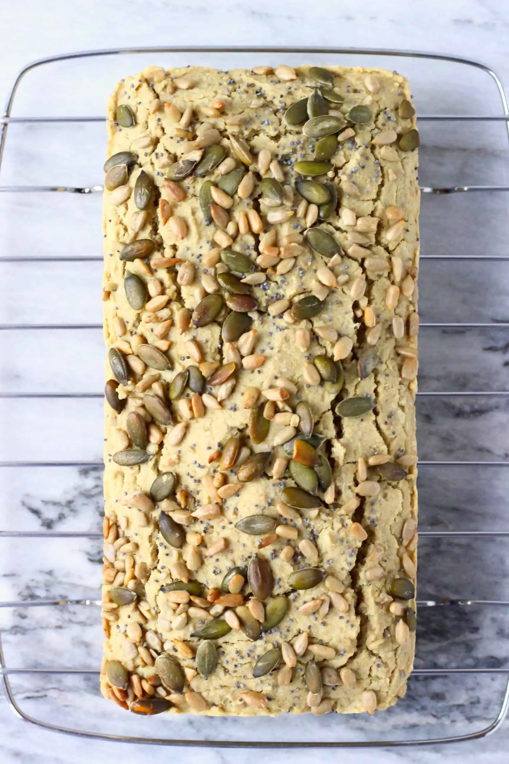 A loaf of sunflower seed bread topped with mixed seeds on a cooling rack 