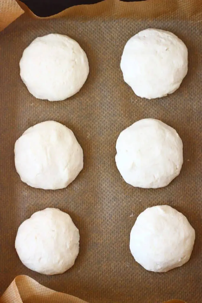 Six raw bread rolls on a sheet of brown baking paper