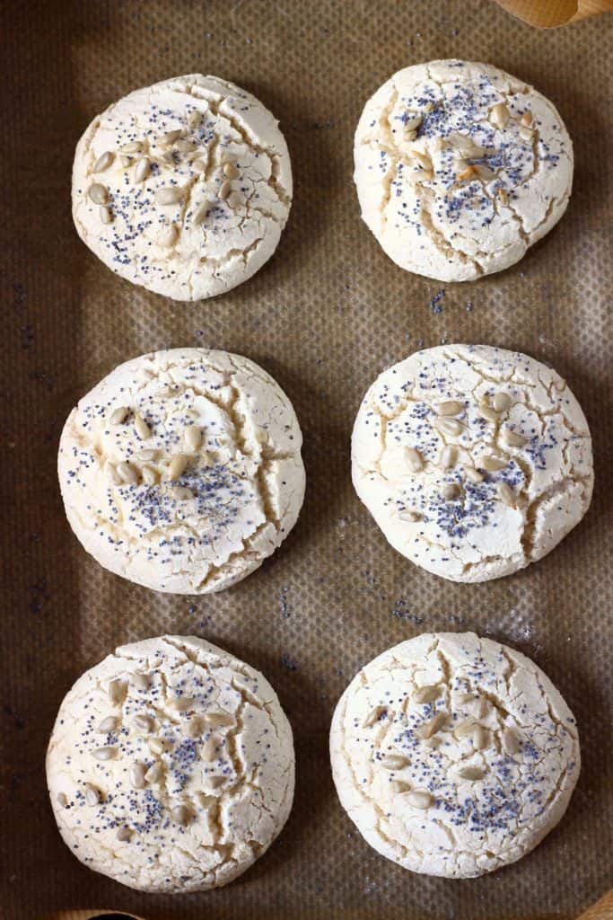 Six bread rolls topped with mixed seeds on a sheet of baking paper
