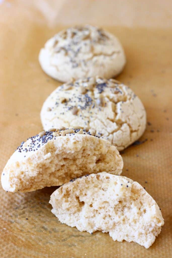 A halved bread roll on a sheet of brown baking paper with two bread rolls in the background