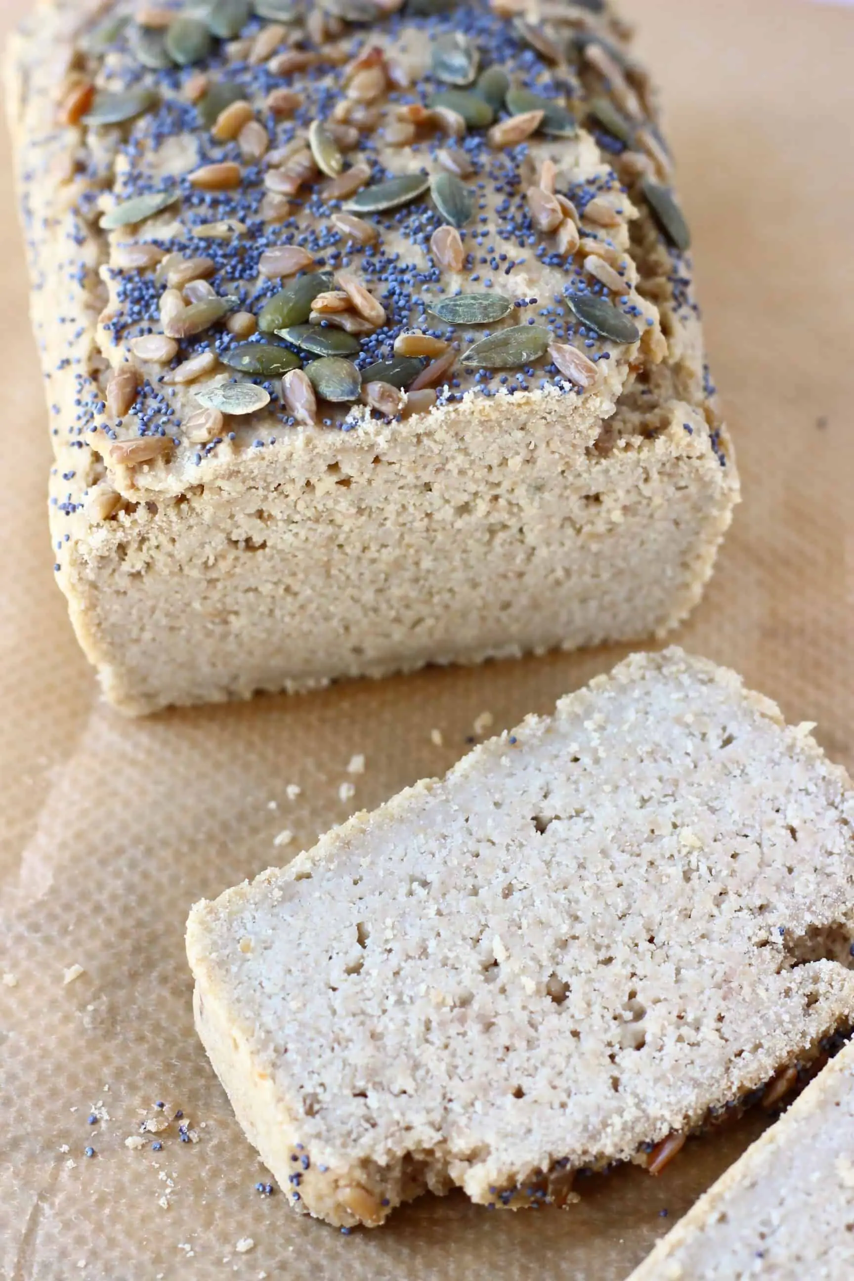A loaf of sunflower seed bread topped with mixed seeds with two slices of bread next to it