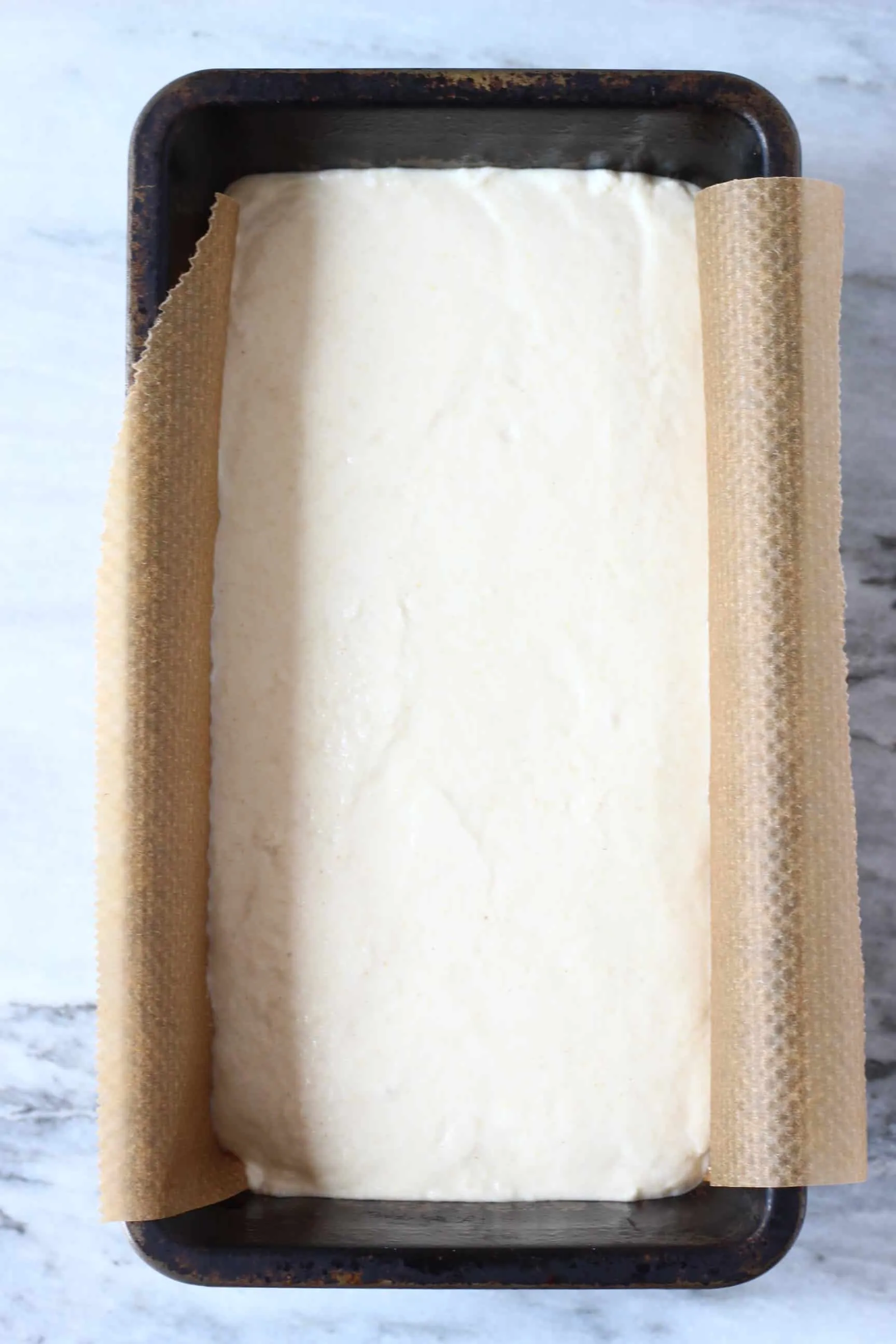 White gluten-free rice bread batter  in a black loaf tin lined with baking paper 