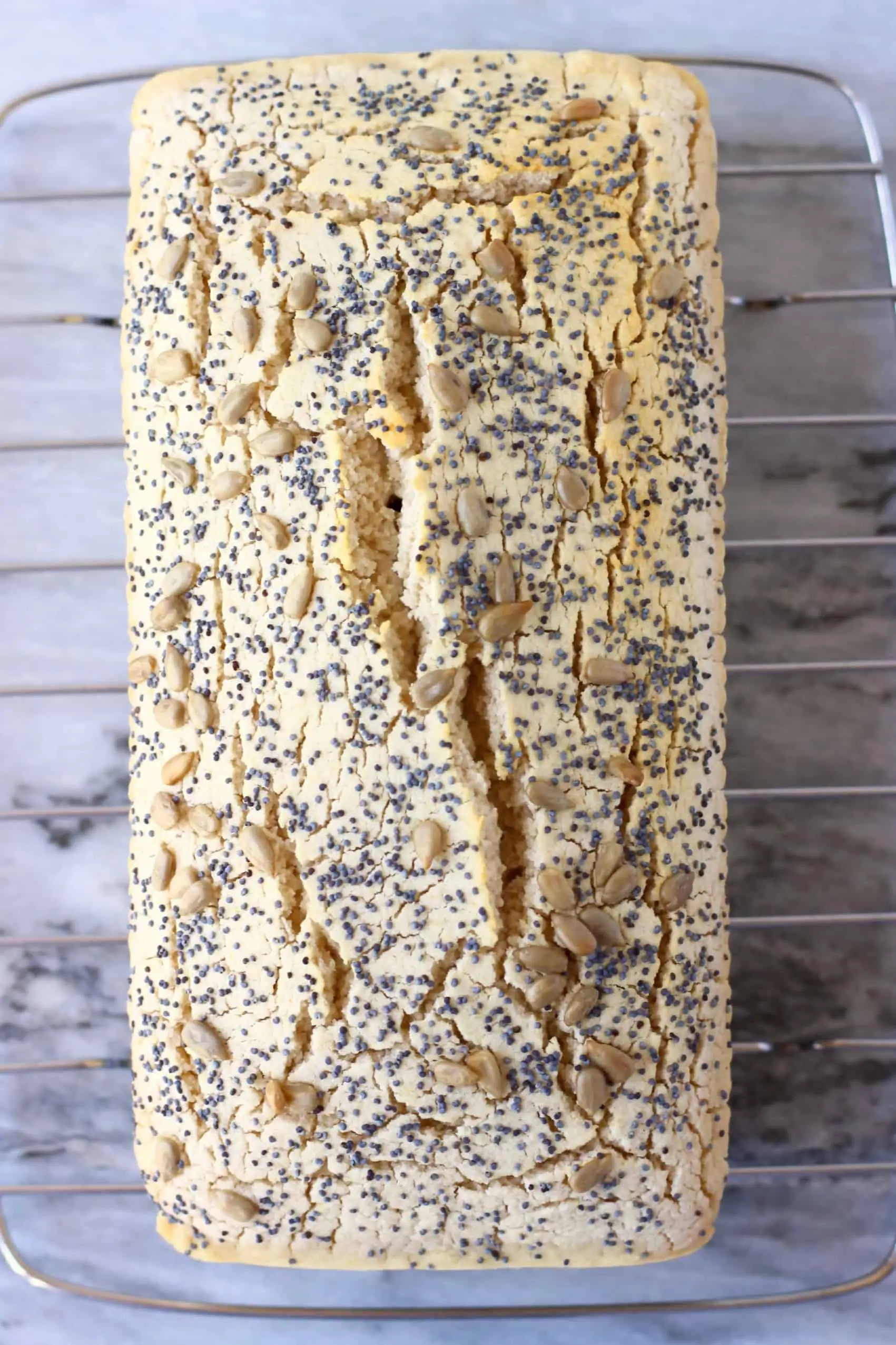 A loaf of gluten-free rice bread topped with mixed seeds on a silver wire rack 