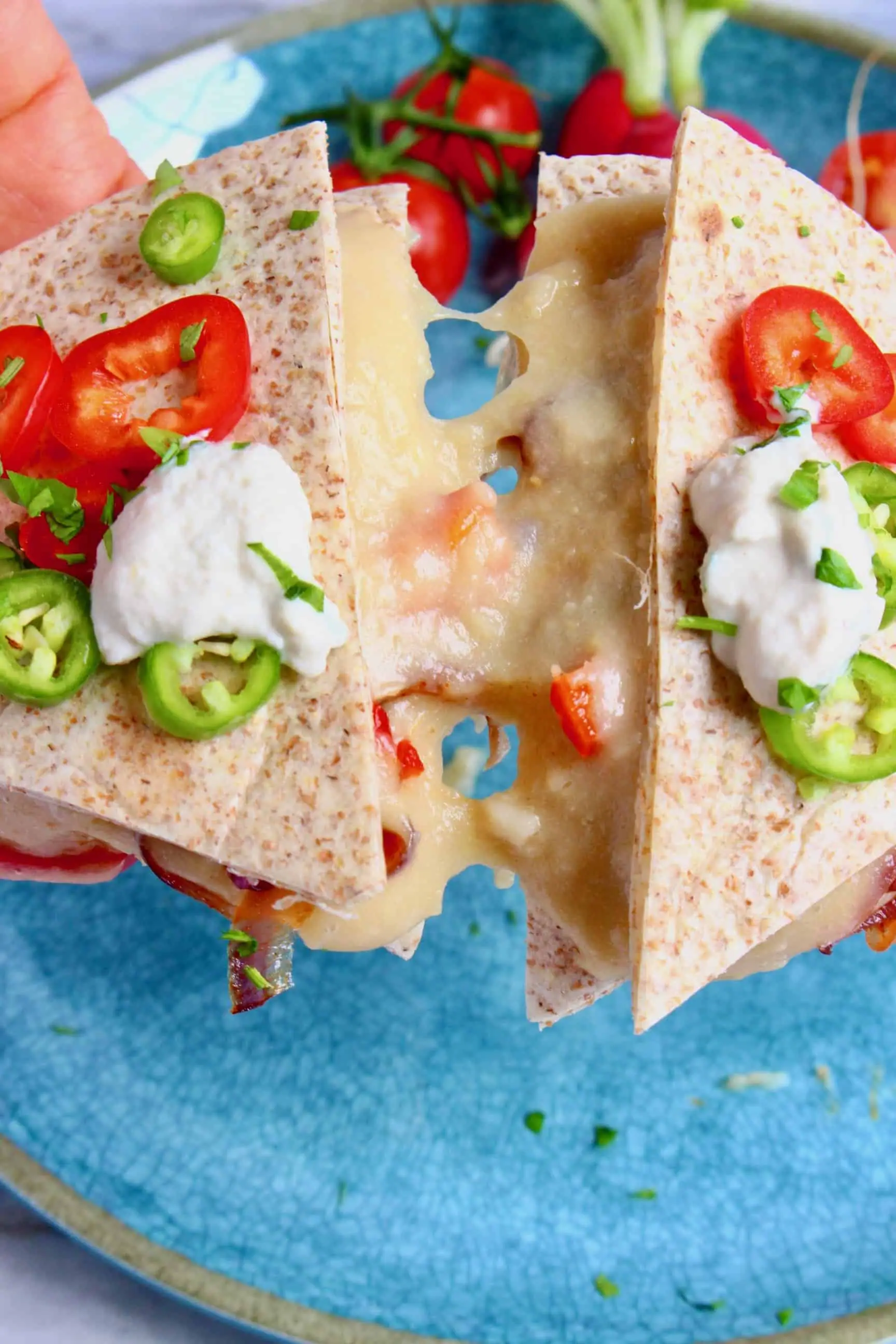 A quesadilla with cheese and vegetables being held up against a blue plate