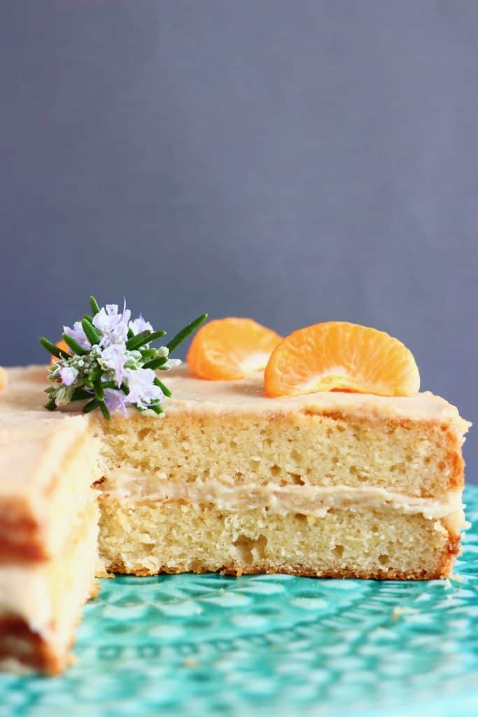 A sponge cake with white buttercream frosting topped with clementine segments on a green cake stand against a grey background