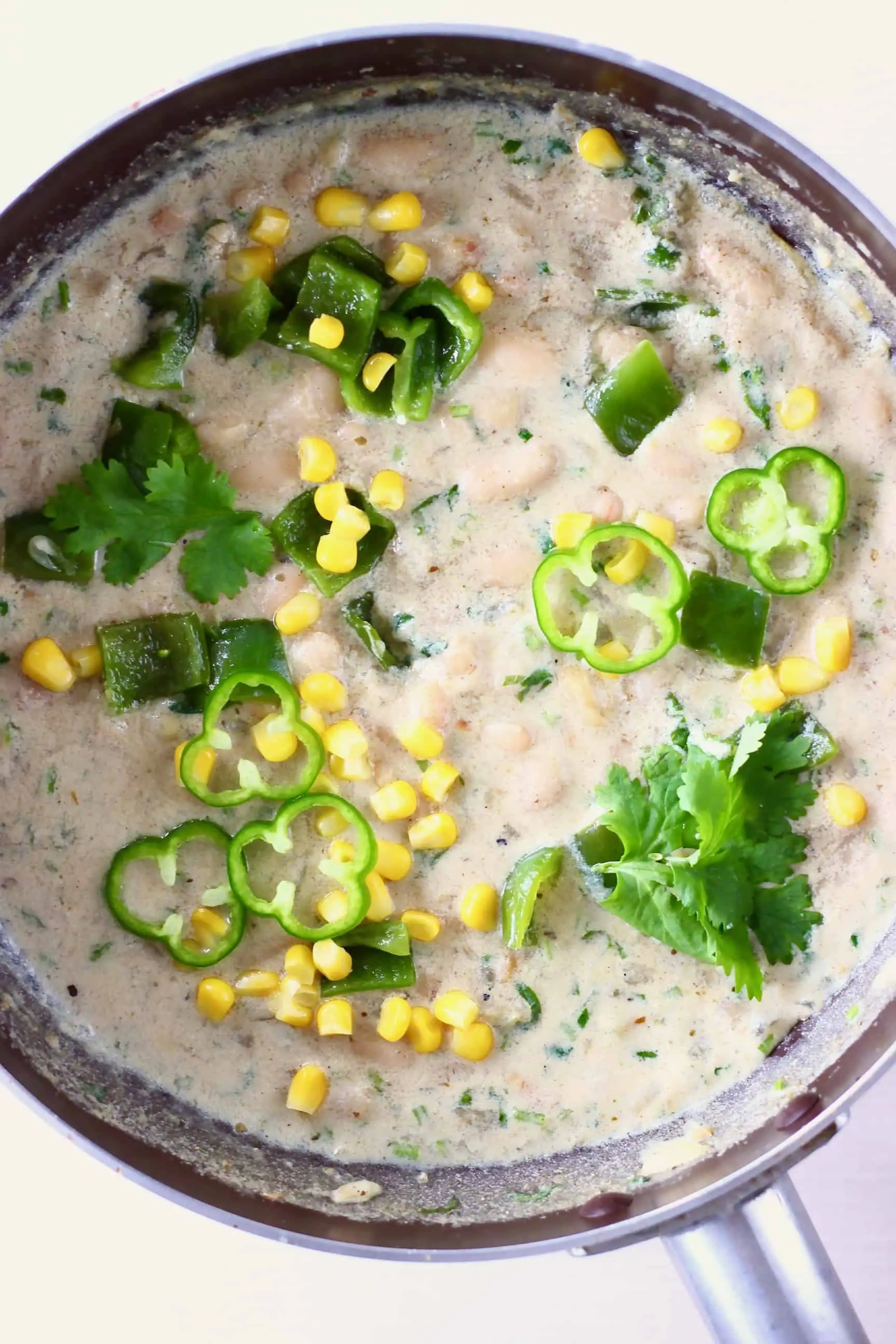 Photo of a saucepan with white stew with white beans, sweetcorn and green pepper