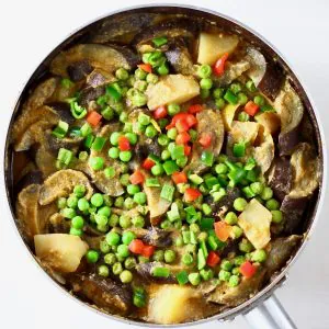 Aubergine, potato and pea curry in a round pan against a white background