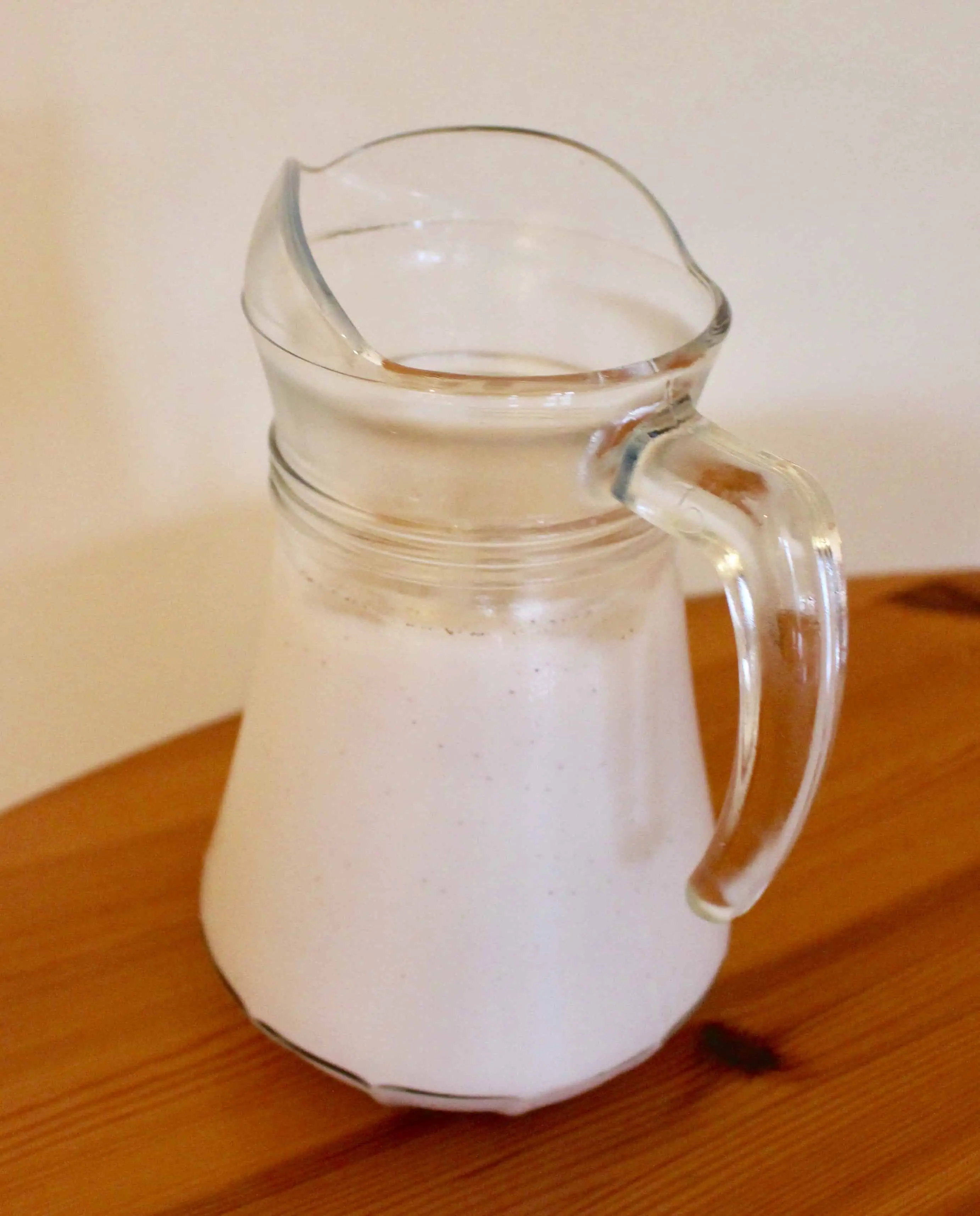 A glass jug of white horchata on a brown wooden table