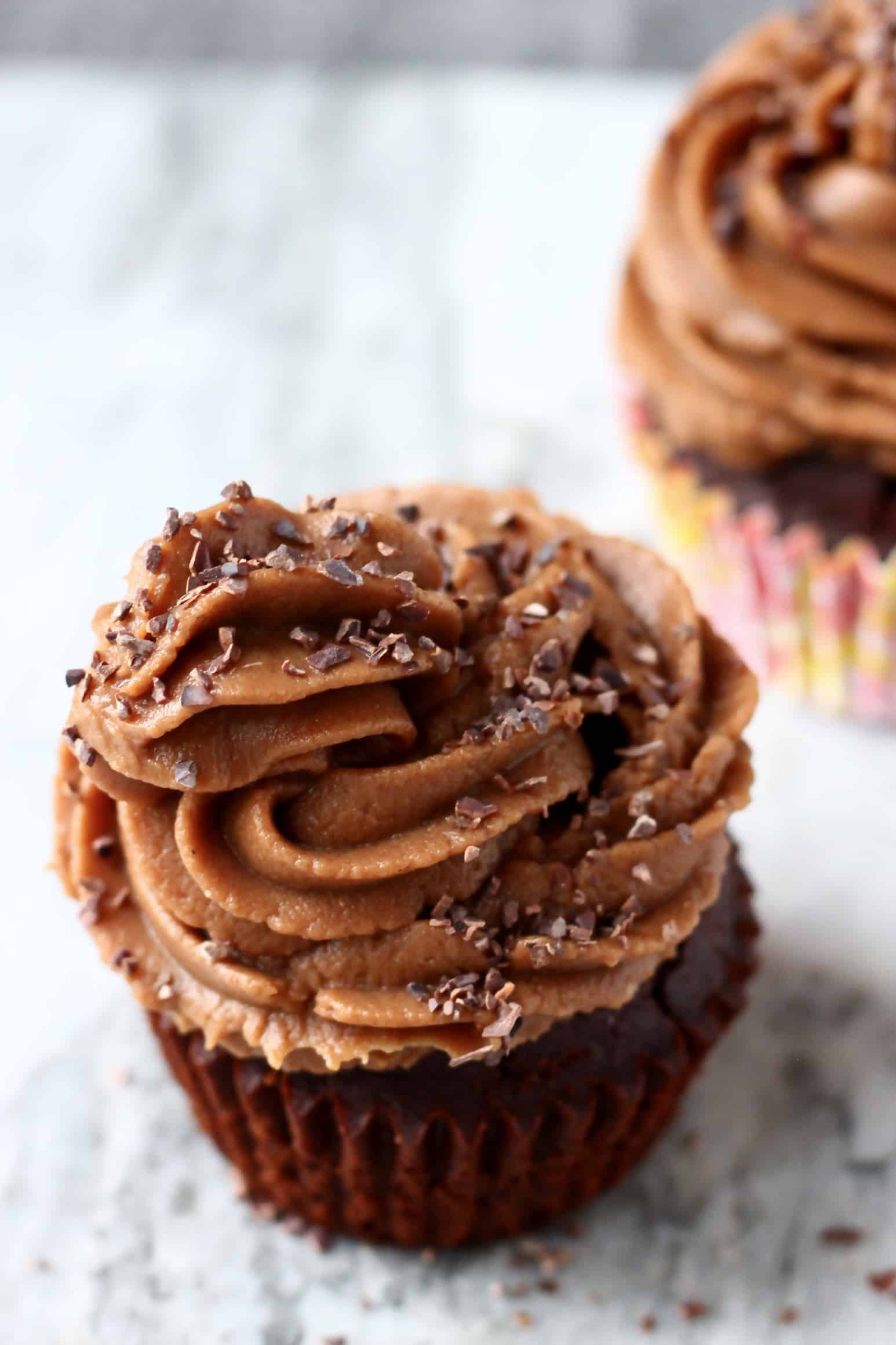 Two gluten-free vegan chocolate cupcakes with chocolate frosting piped on top