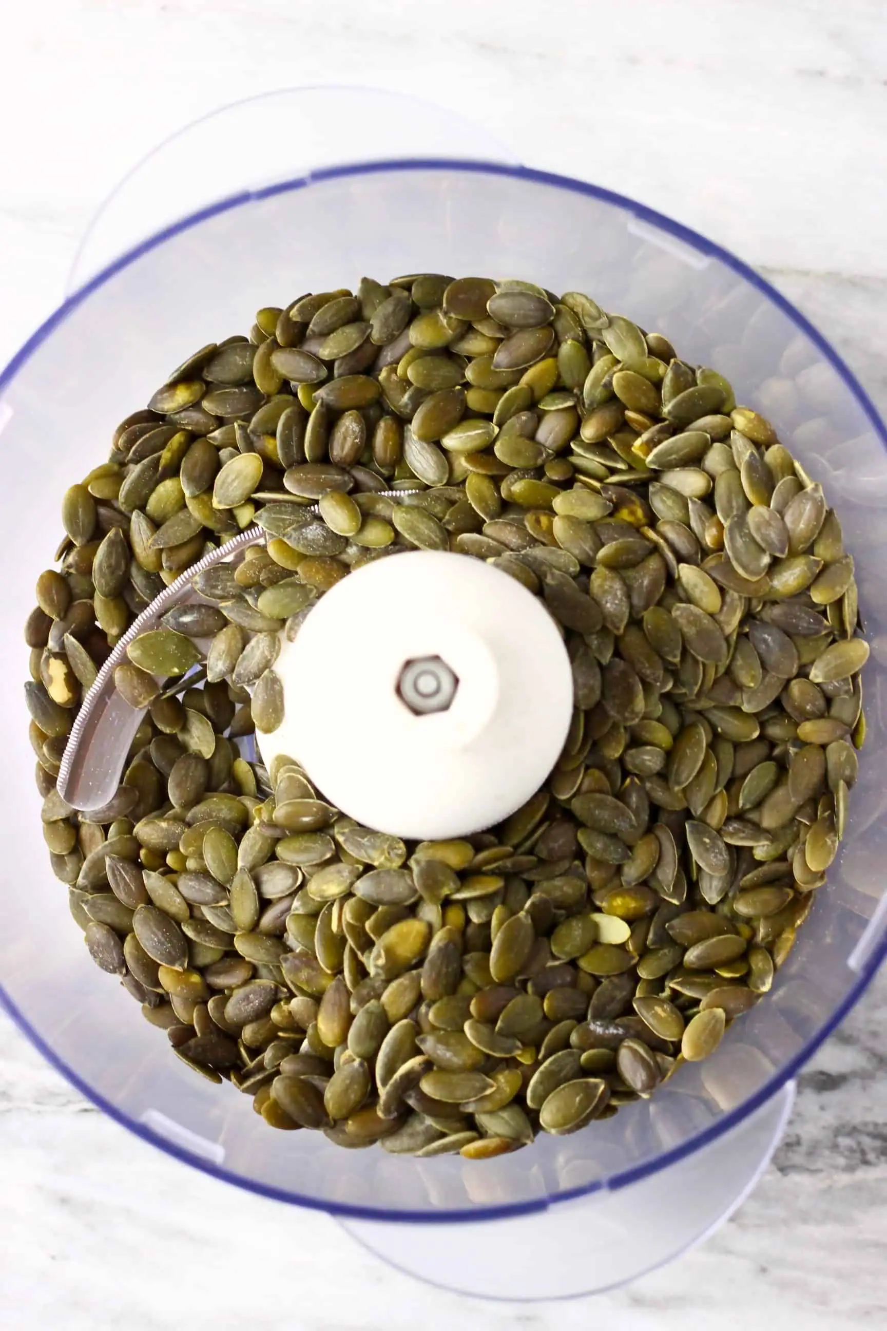 Pumpkin seeds in a food processor against a marble background