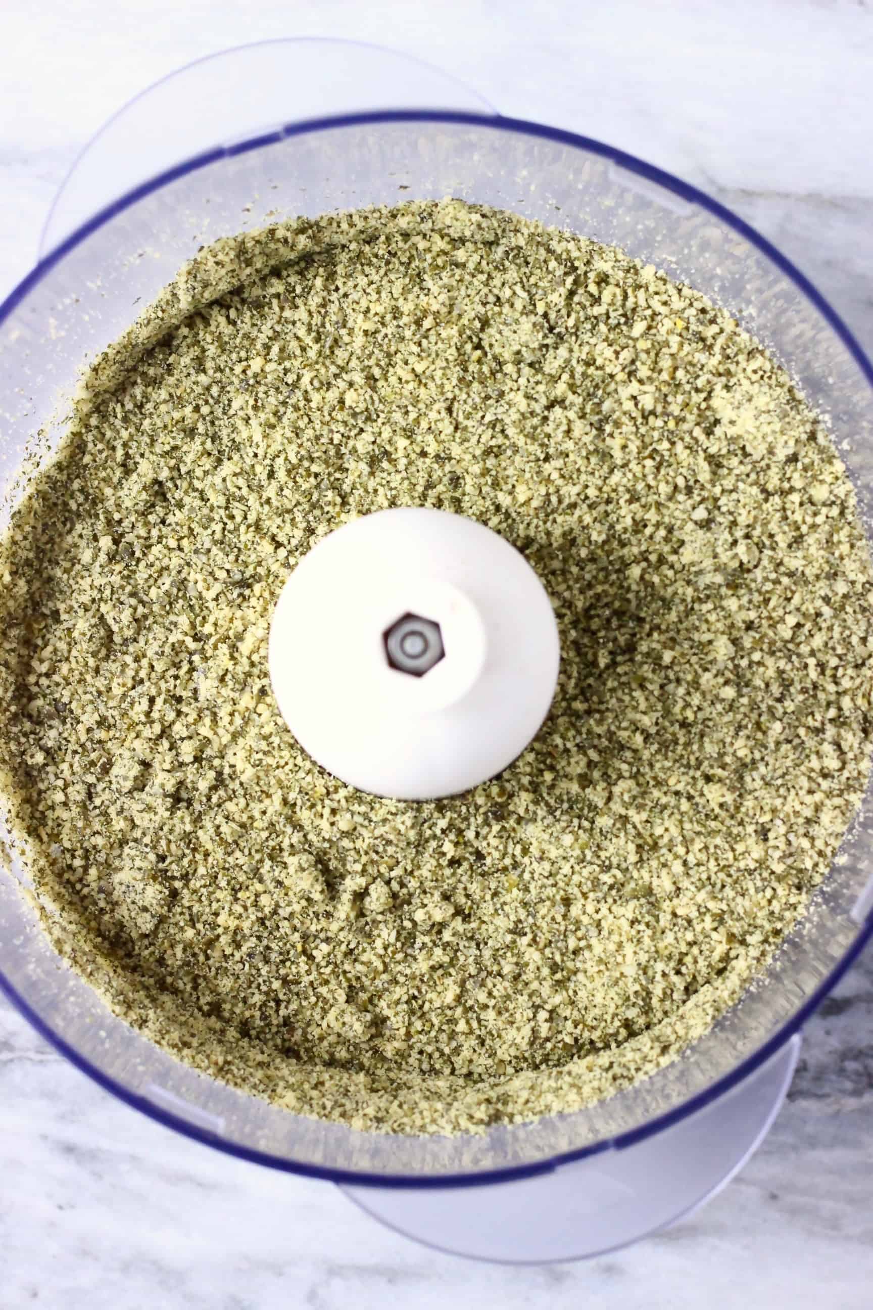 Ground pumpkin seeds in a food processor against a marble background