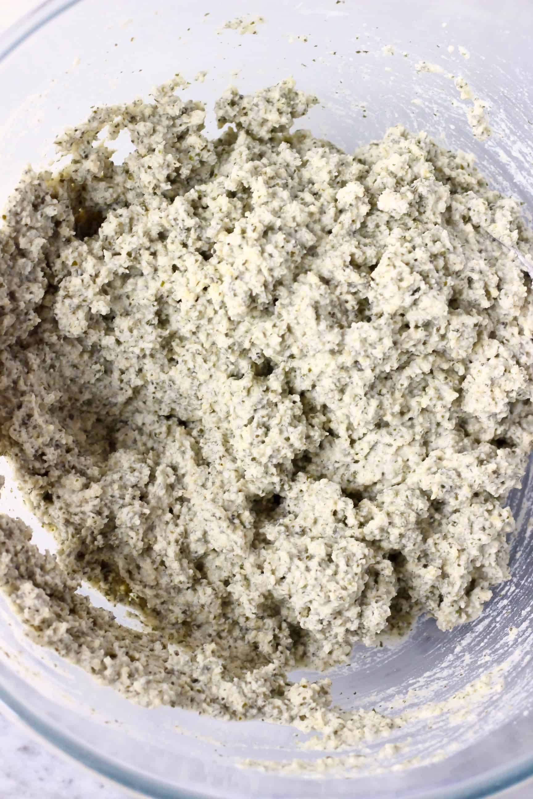 Pumpkin seed bread batter in a glass mixing bowl against a marble background