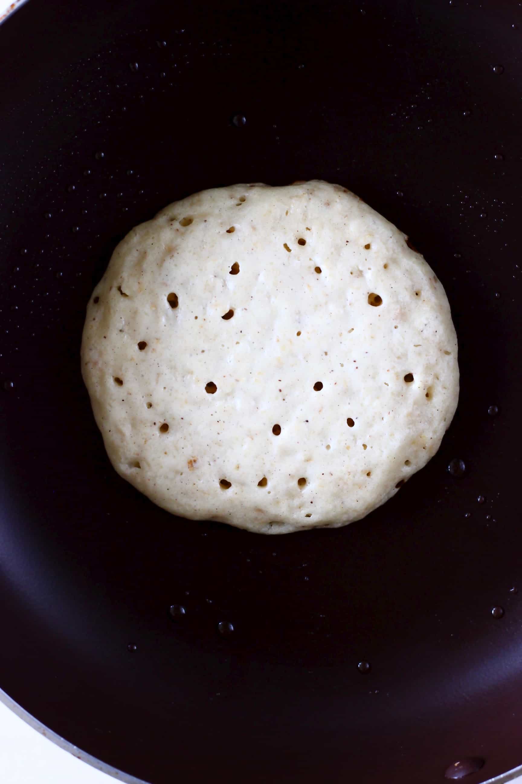 A half-cooked gluten-free vegan oatmeal pancake being cooked in a frying pan 