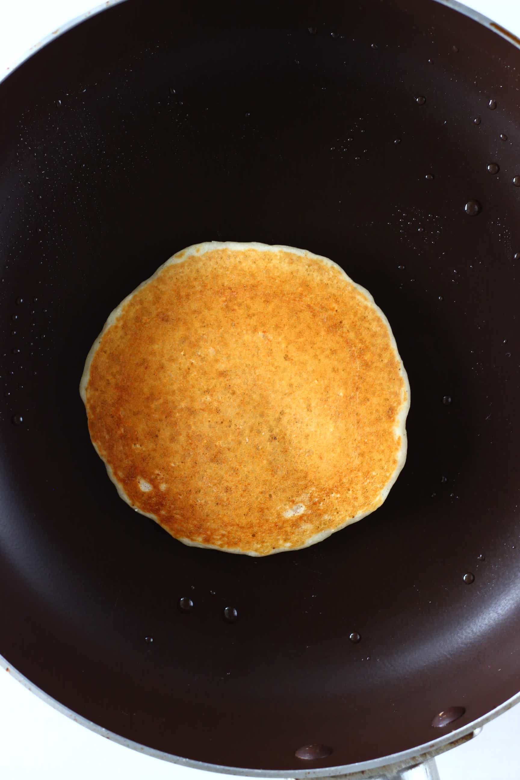 A golden brown gluten-free vegan oatmeal pancake being cooked in a frying pan