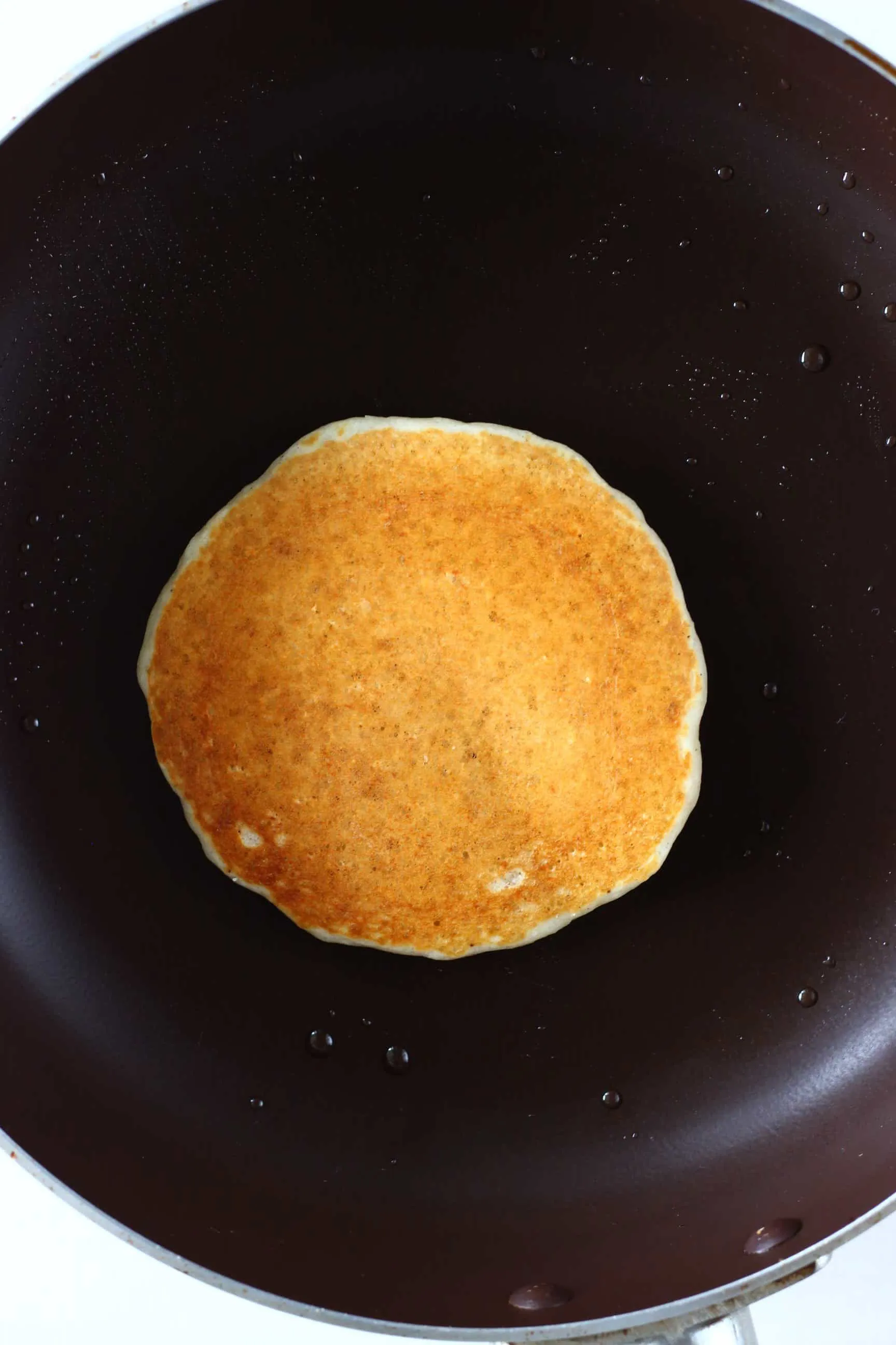 A golden brown gluten-free vegan oatmeal pancake being cooked in a frying pan 