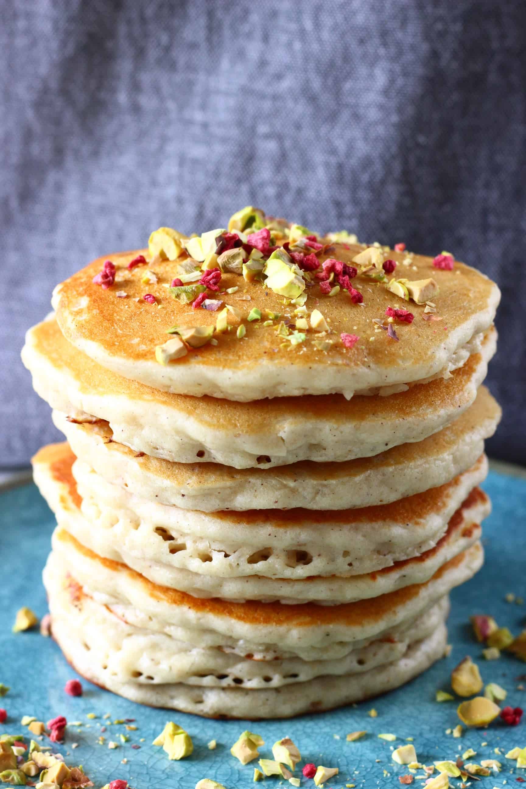 A stack of gluten-free vegan oatmeal pancakes on a plate sprinkled with chopped pistachios and freeze-dried raspberries 