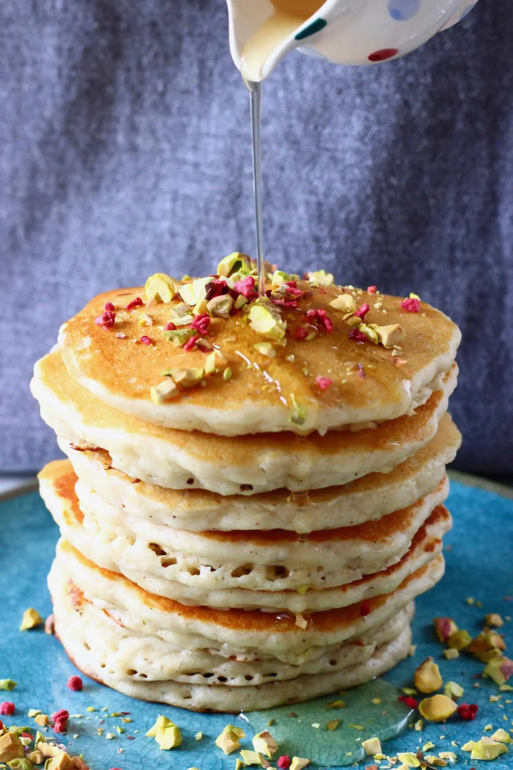 A stack of gluten-free vegan oatmeal pancakes on a plate with syrup being poured over the top from a small jug