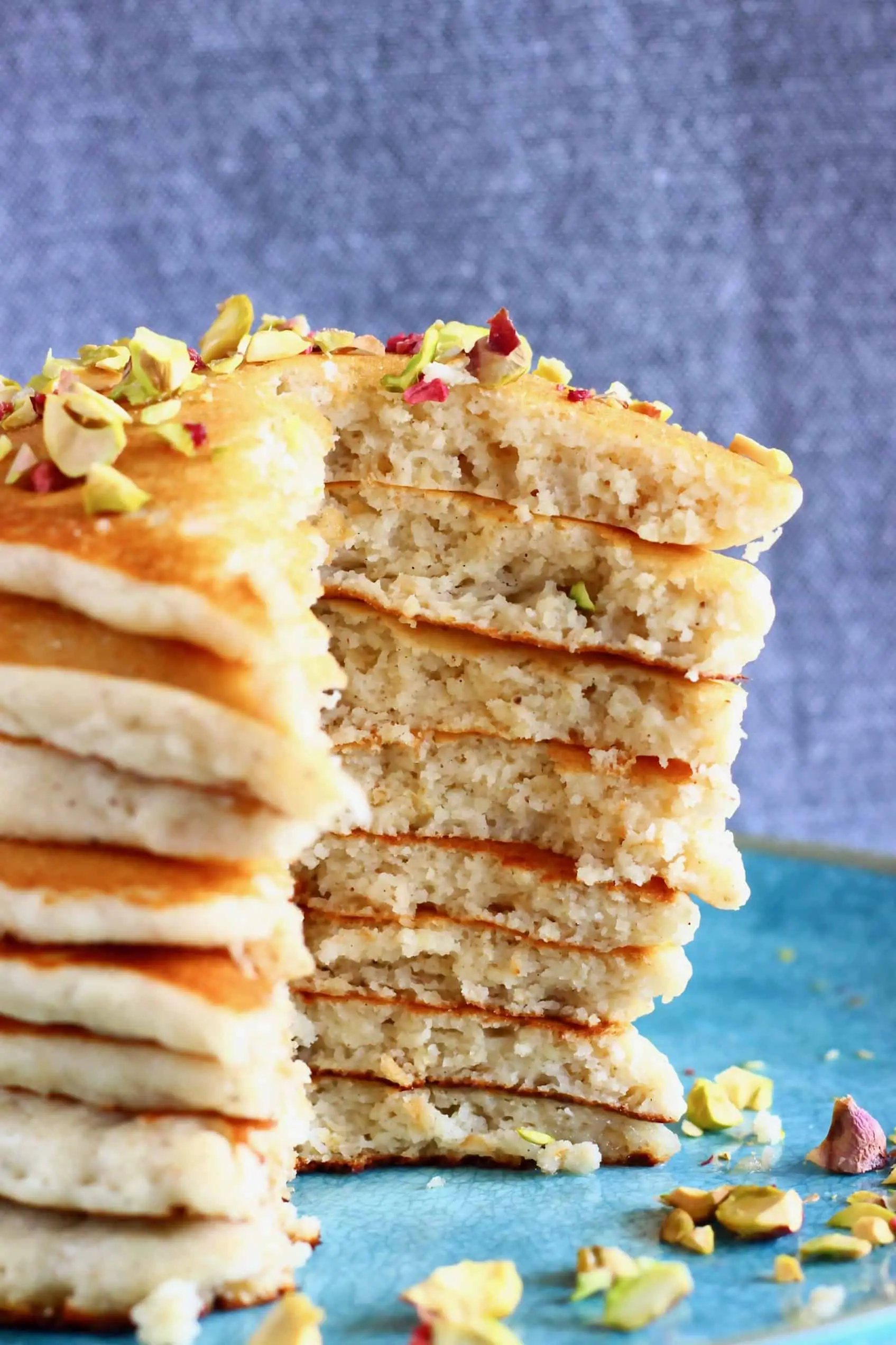 A stack of sliced gluten-free vegan oatmeal pancakes on a plate topped with chopped pistachios