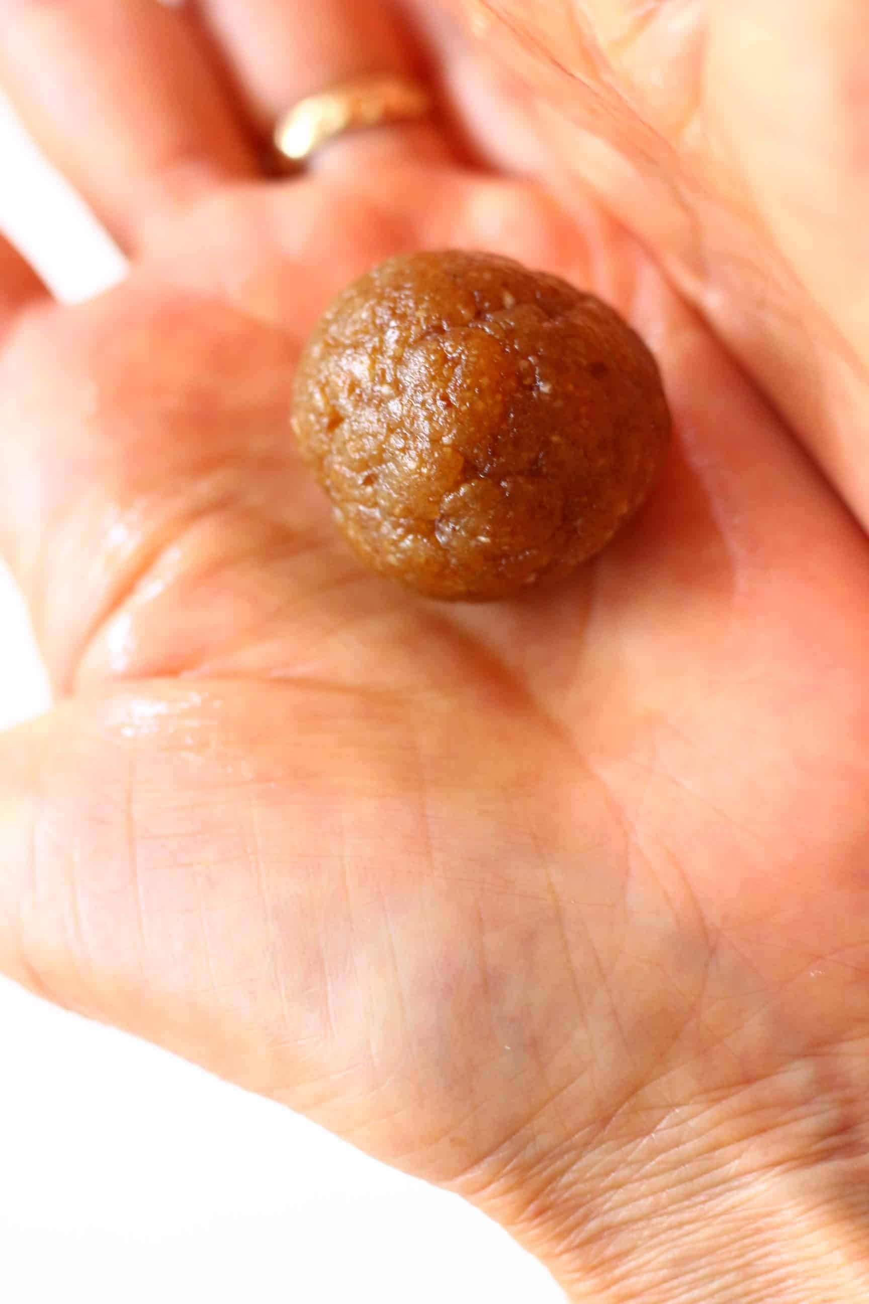 A round brown vegan energy ball being rolled between two hands