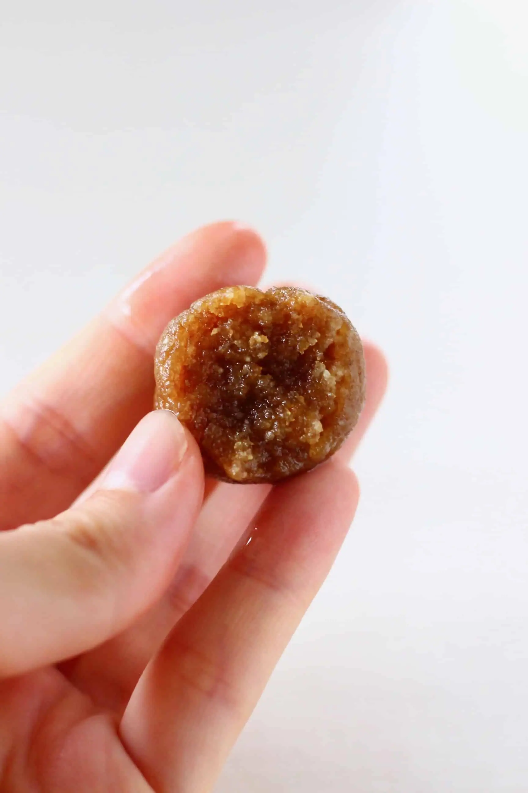 A round brown vegan energy ball with a bite taken out of it being held up