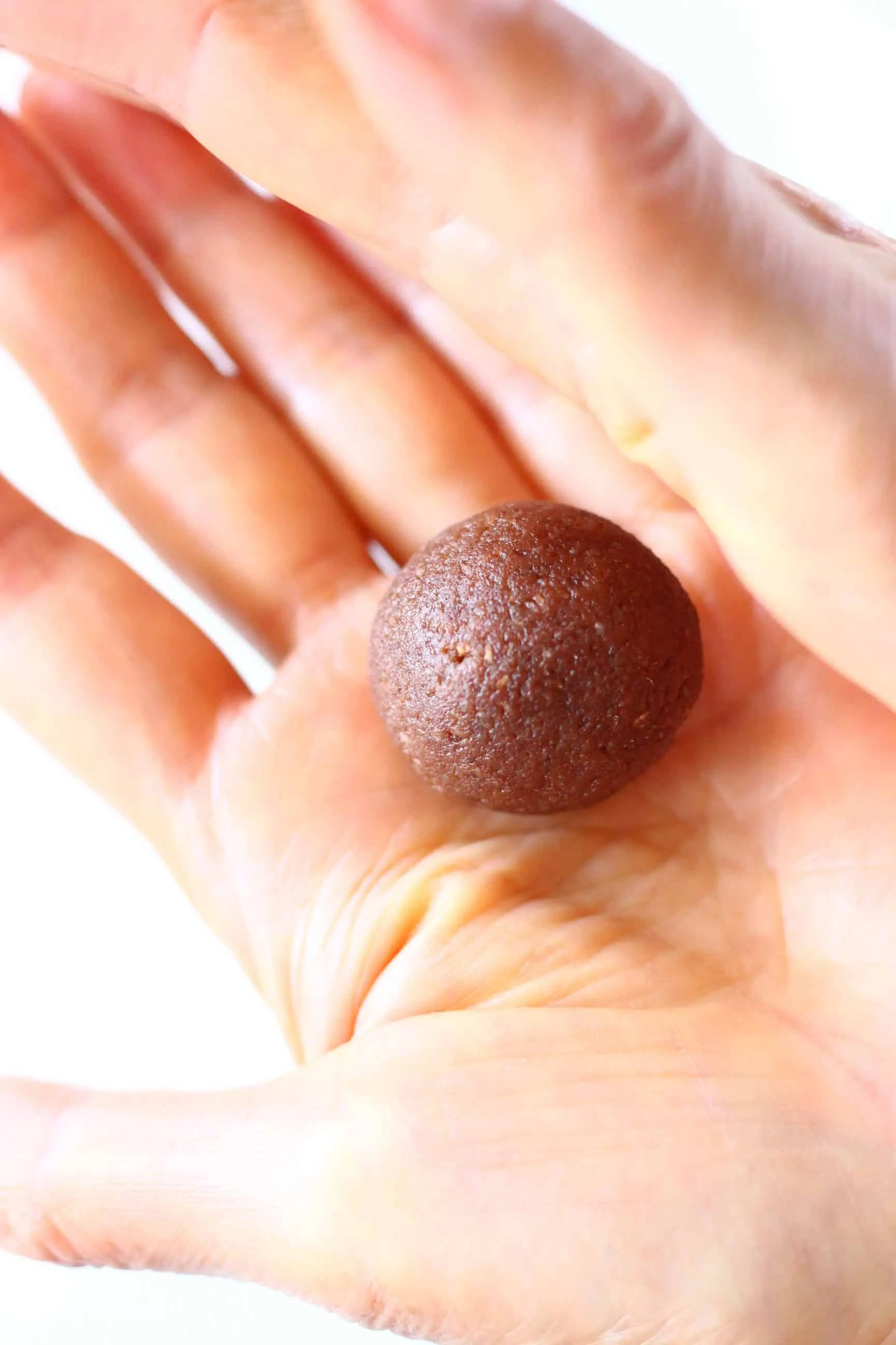 A round vegan protein ball being rolled between two hands