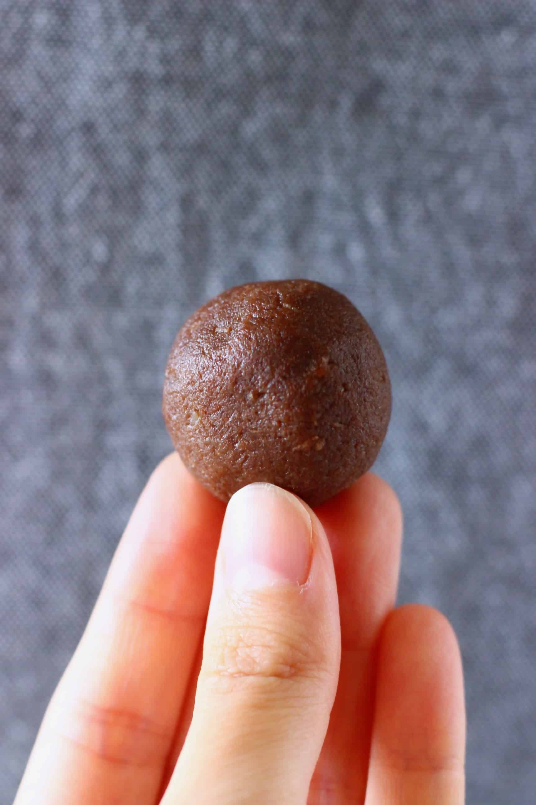 A round vegan protein ball being held up with a hand against a grey background