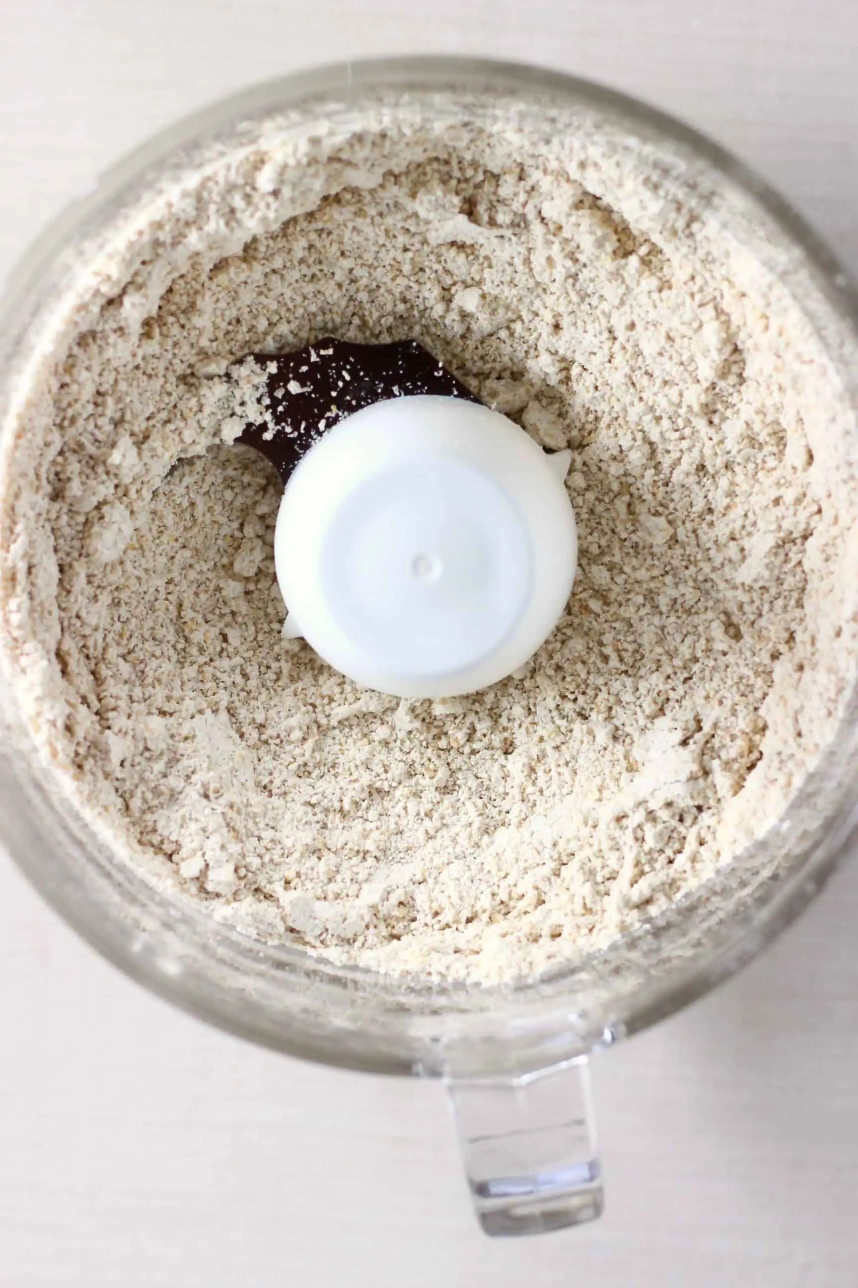 Oat flour in a food processor against a white background