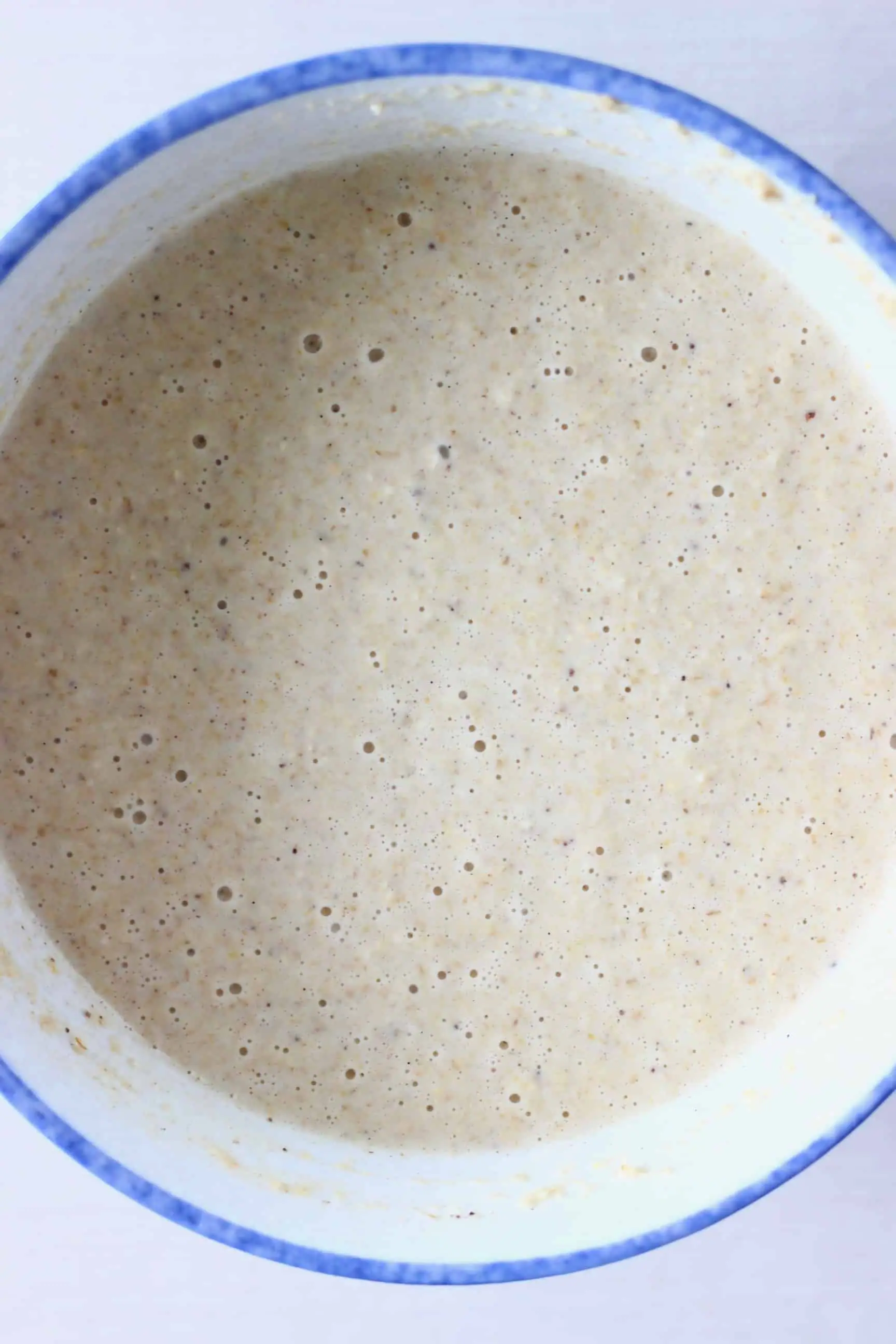 Raw oat flour pancake batter in a white bowl with a blue rim against a white background
