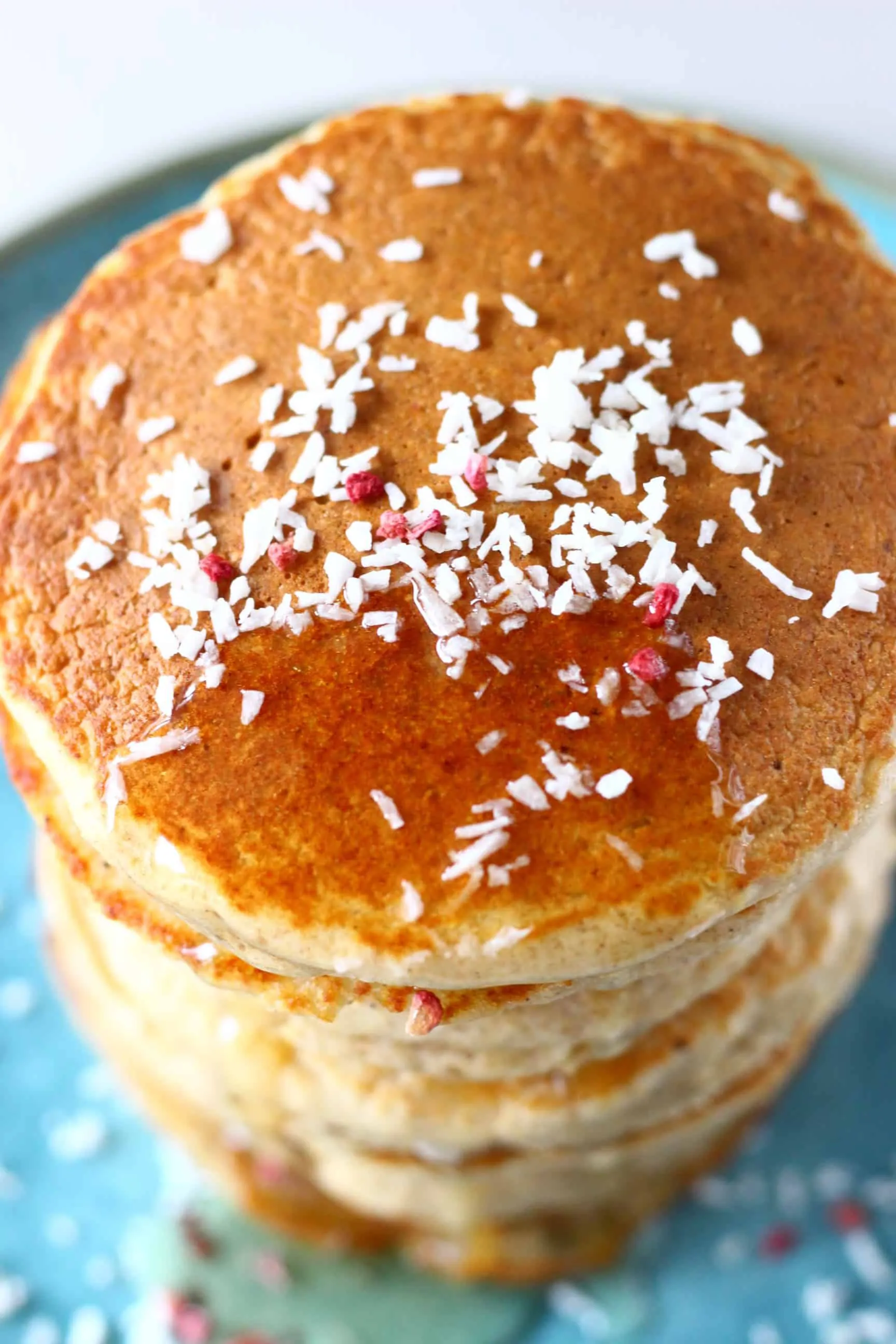 A stack of oat flour pancakes topped with desiccated coconut and syrup on a blue plate