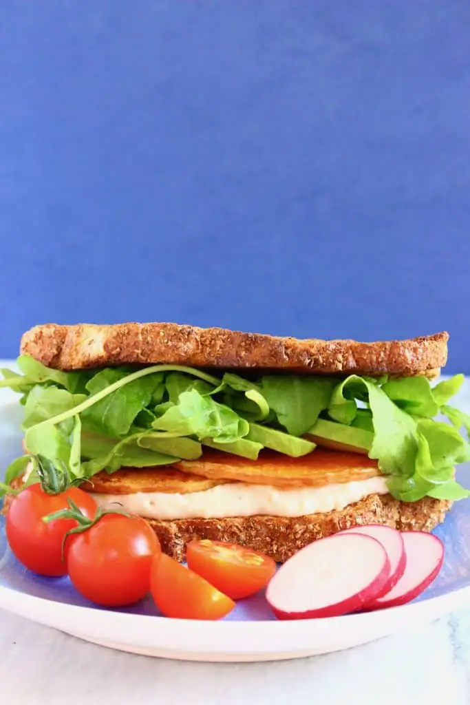 Hummus, butternut squash and lettuce sandwich on a light blue plate against a dark blue background
