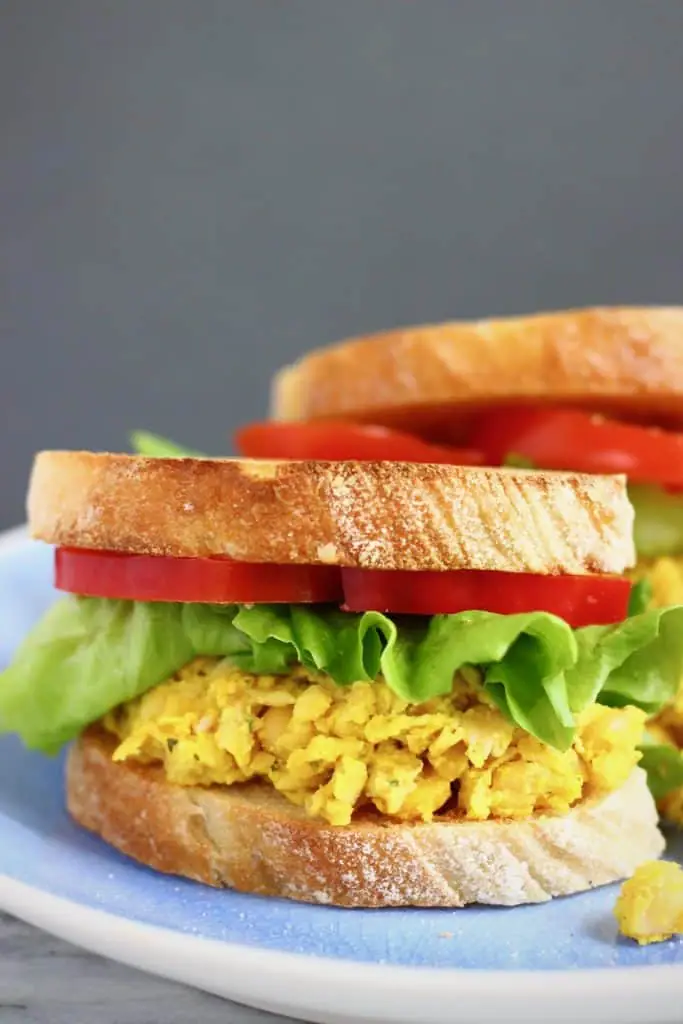 Yellow mashed chickpeas, lettuce and red pepper in sandwiches on a blue plate against a grey background