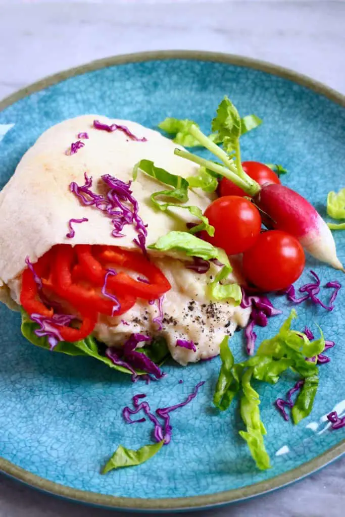 A halved pitta filled with mashed white beans and salad on a blue plate against a marble background