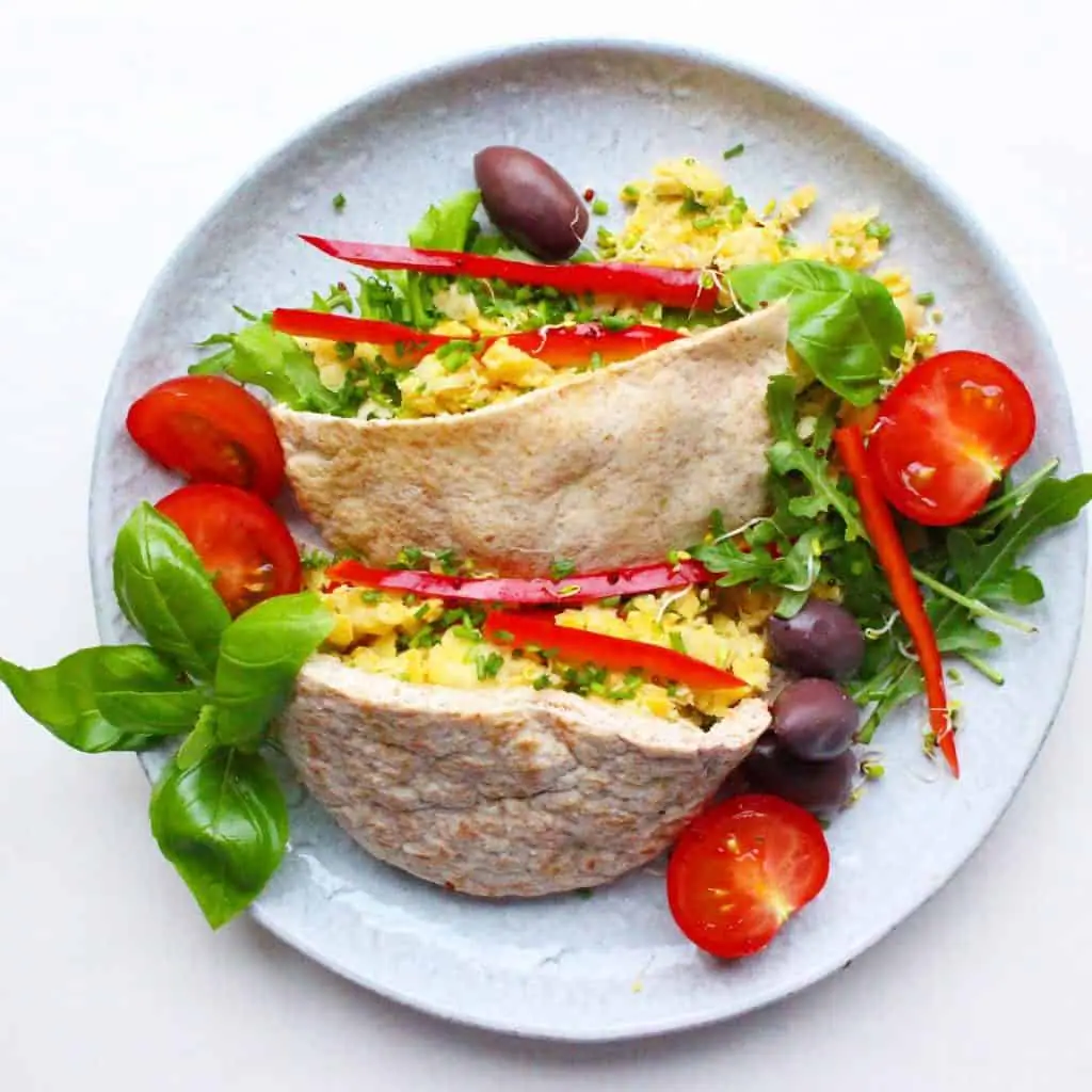 Two pitta halves filled with mashed chickpeas and salad on a grey plate against a white background