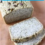 A loaf of pumpkin seed bread with two slices next to it against a sheet of brown baking paper