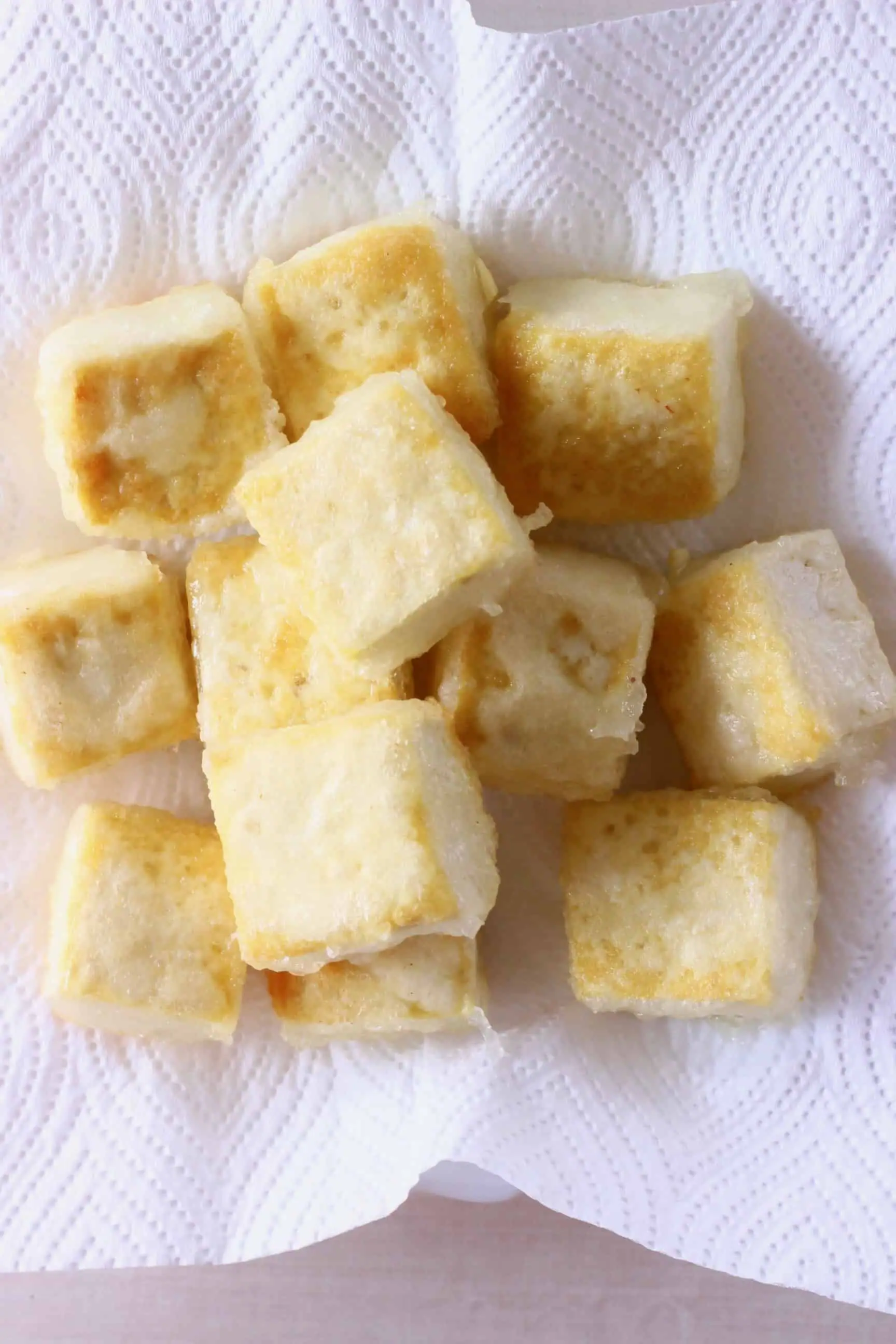 Golden brown cubes of batter-coated tofu on a piece of kitchen paper on a plate