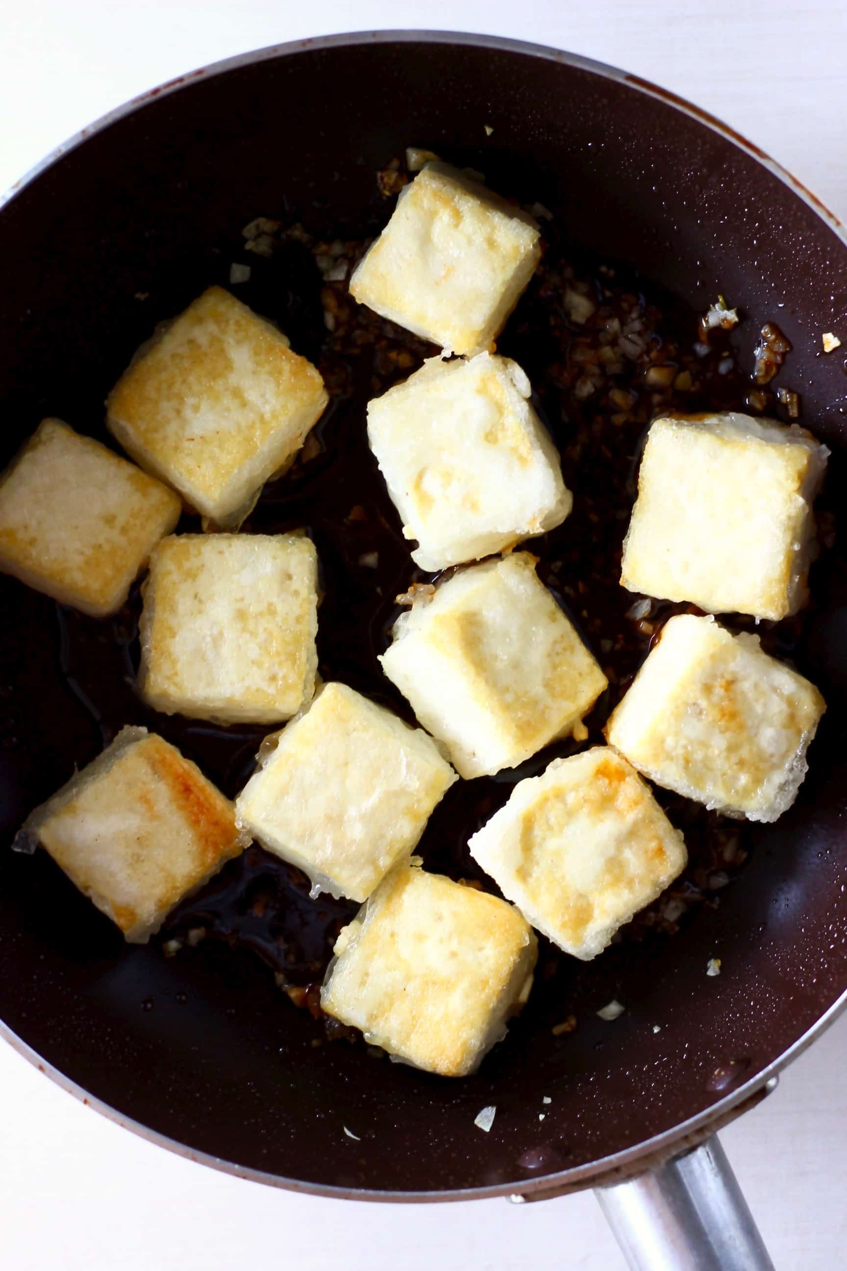 Golden brown cubes of batter-coated tofu in a frying pan 