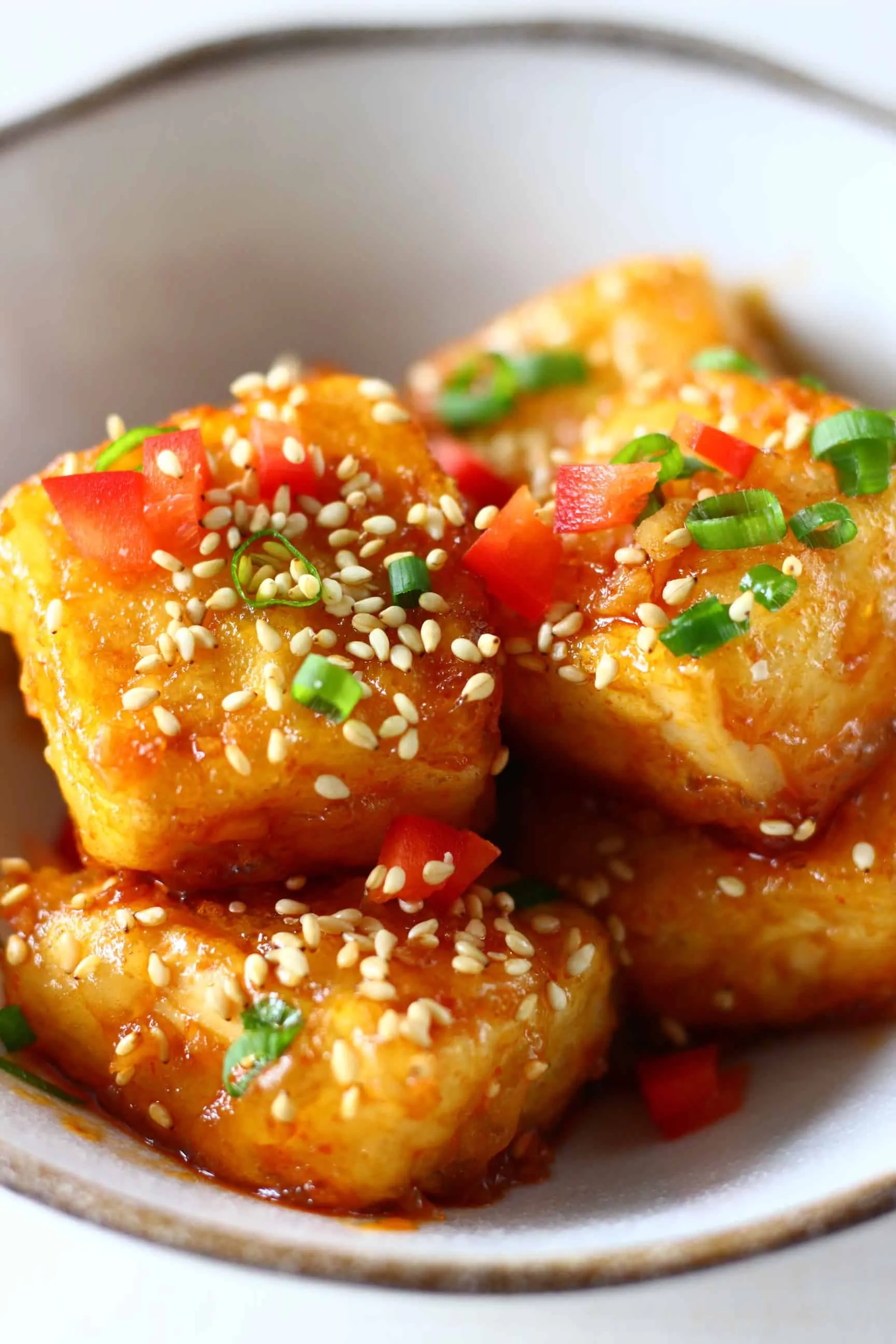 Cubes of spicy tofu sprinkled with sesame seeds, sliced spring onions and chilli in a white bowl 