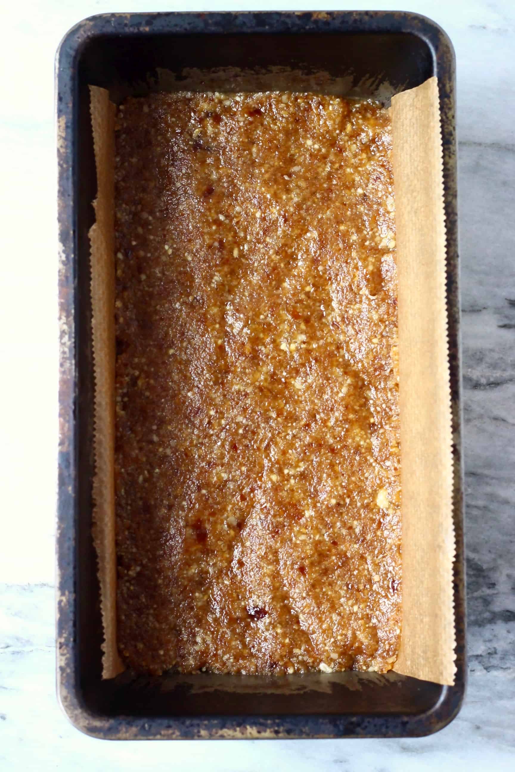 Brown energy bar mixture in a loaf tin lined with baking paper