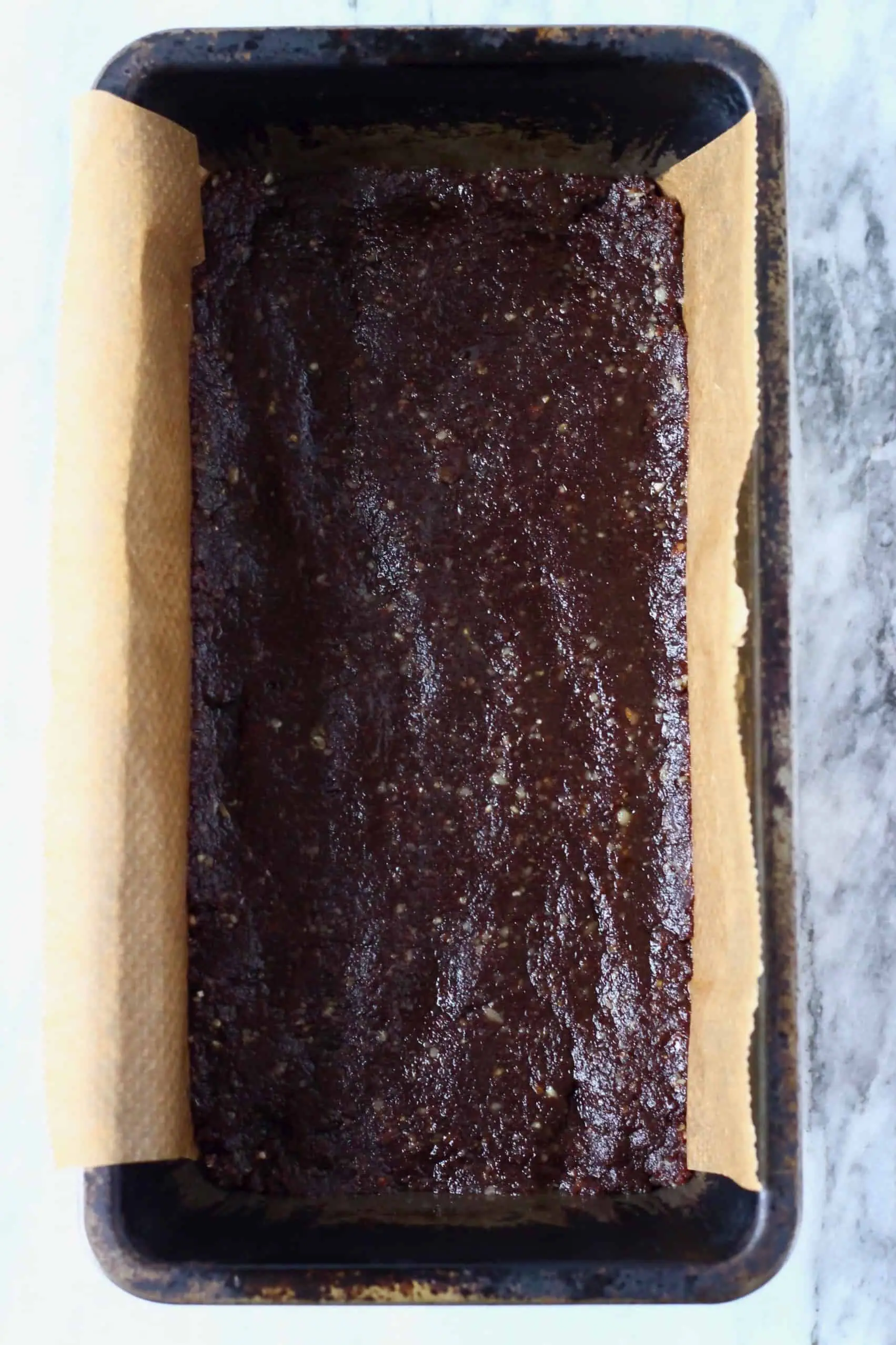 Chocolate no-bake vegan brownie mixture in a loaf tin lined with baking paper