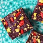 Three square no-bake vegan brownies topped with goji berries and chopped pistachios on a plate