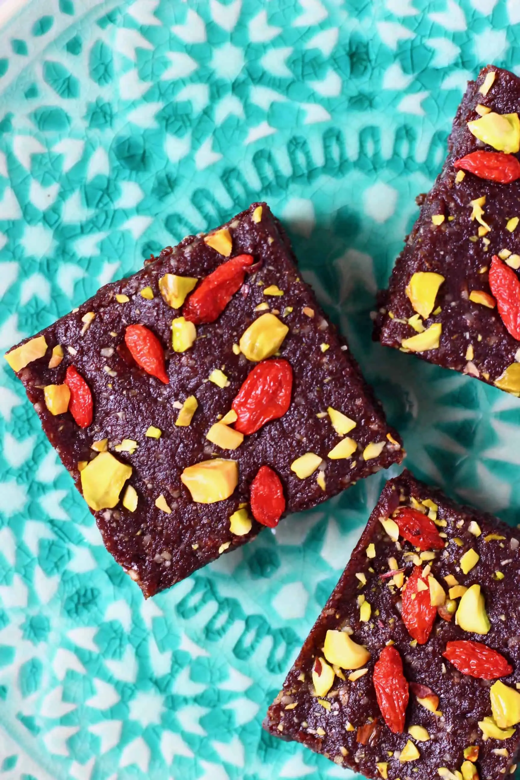 Three square no-bake vegan brownies topped with goji berries and chopped pistachios on a plate