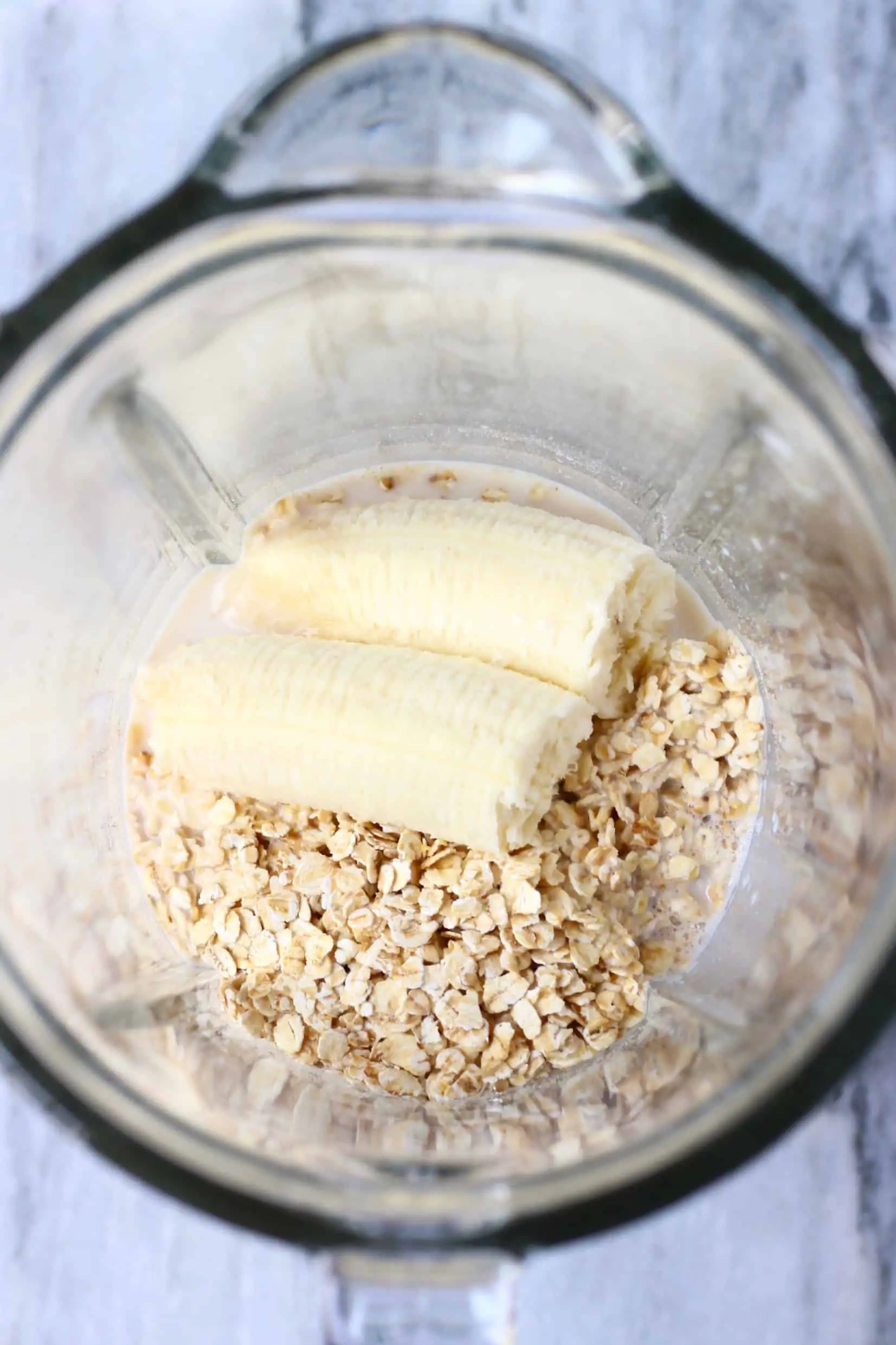 Oats, banana and almond milk in a blender against a marble background