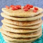 A stack of banana oatmeal pancakes decorated with goji berries on a green plate against a grey background