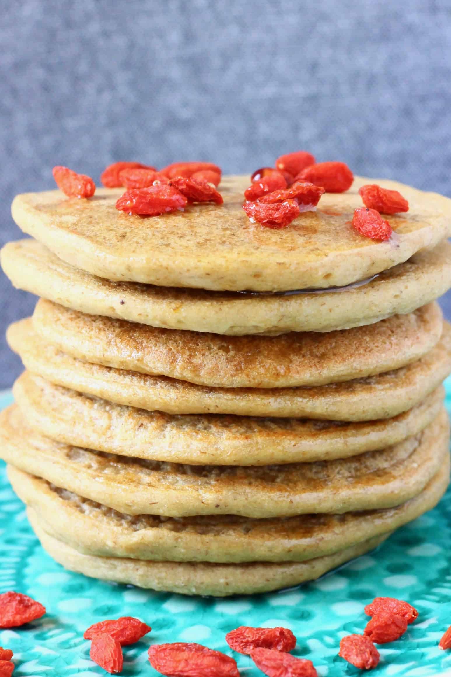 A stack of banana oatmeal pancakes decorated with goji berries on a green plate against a grey background