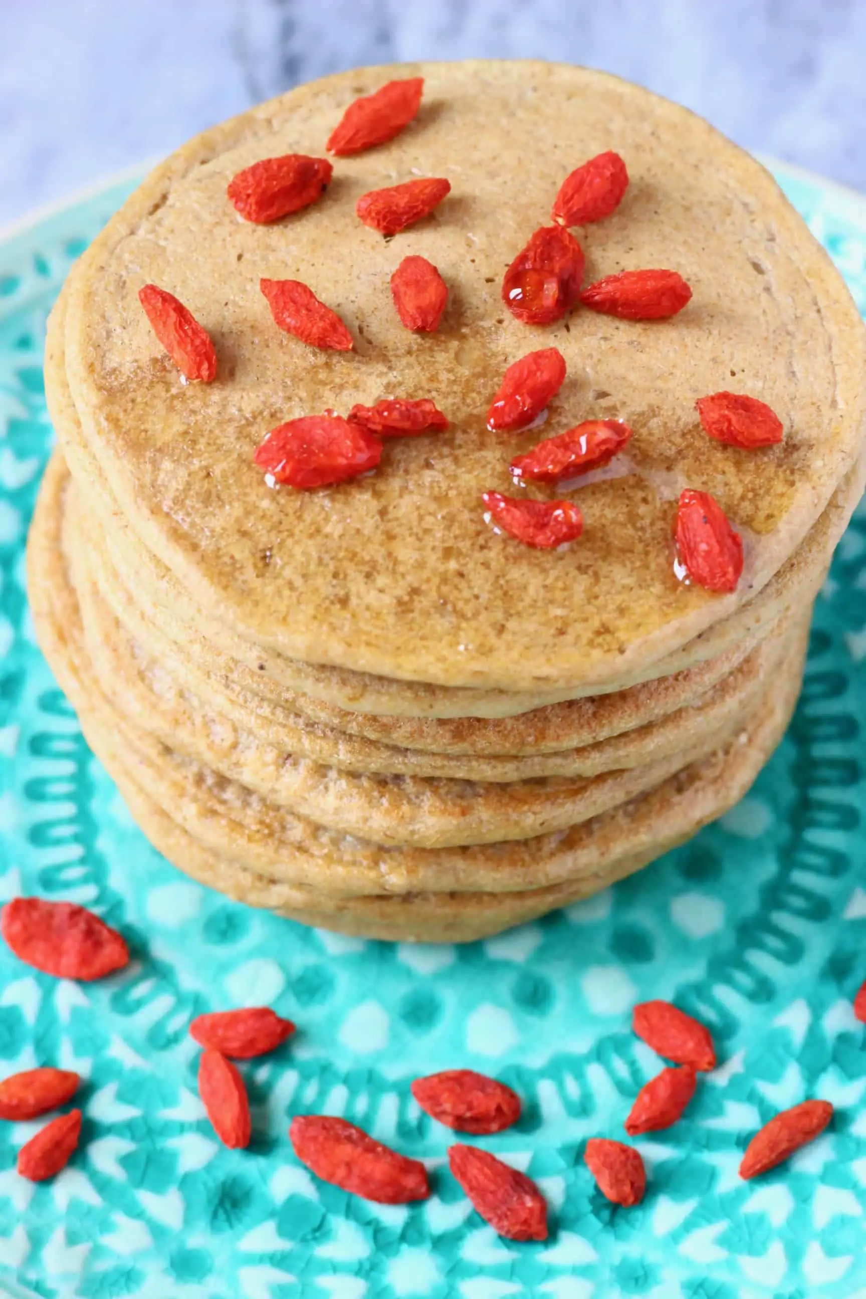 A stack of banana oatmeal pancakes decorated with goji berries on a green plate against a marble background