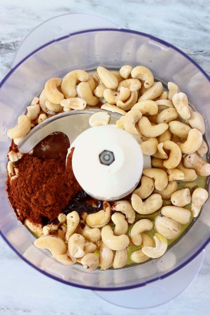 Cashew nuts, cocoa powder, agave syrup and melted cacao butter in a food processor against a marble background