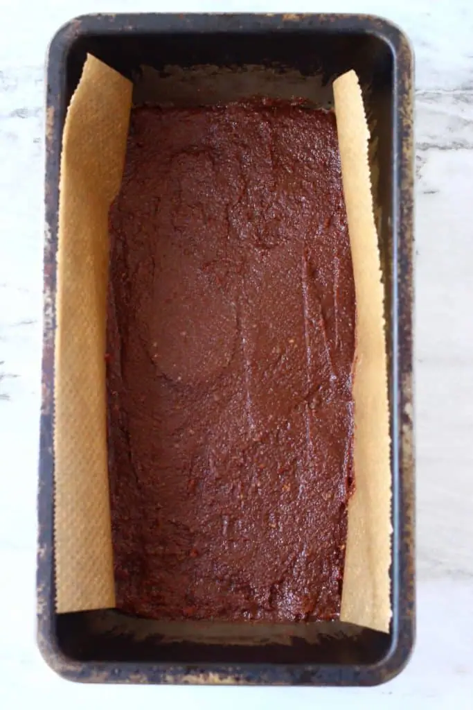 Chocolate bar mixture in a black loaf tin lined with brown baking paper against a marble background