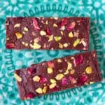 Two chocolate bars topped with rose petals and chopped pistachios on a green plate