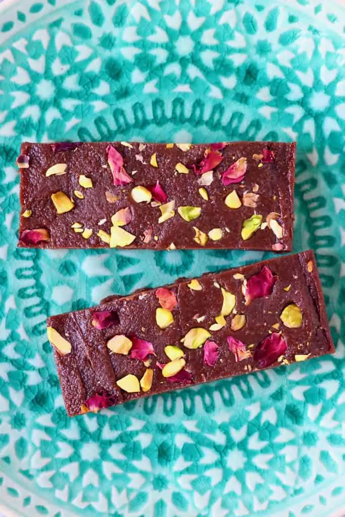 Two chocolate bars topped with rose petals and chopped pistachios on a green plate
