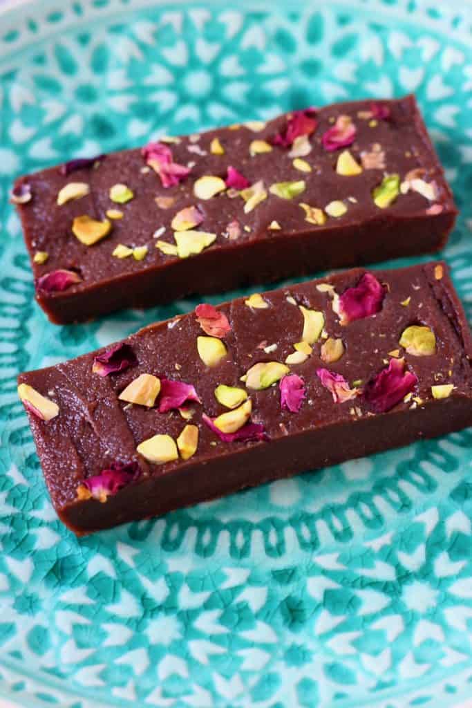 Two chocolate bars topped with rose petals and chopped pistachios on a green plate